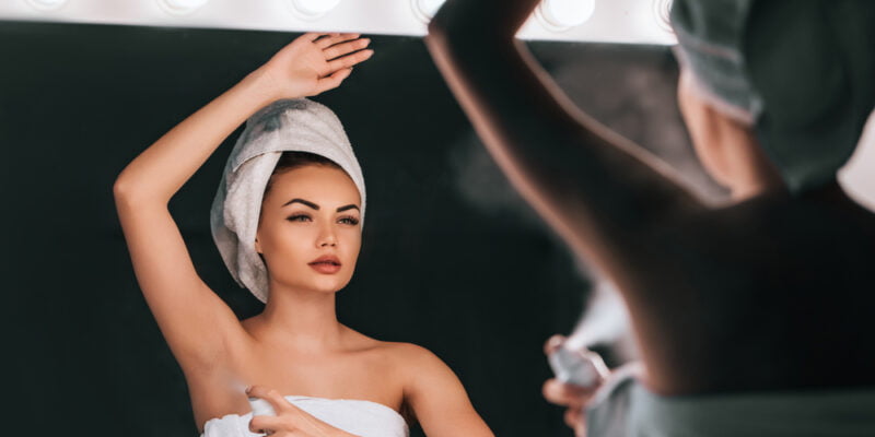 Attractive young woman in bathroom after shower is standing in front of mirror with deodorant in hands