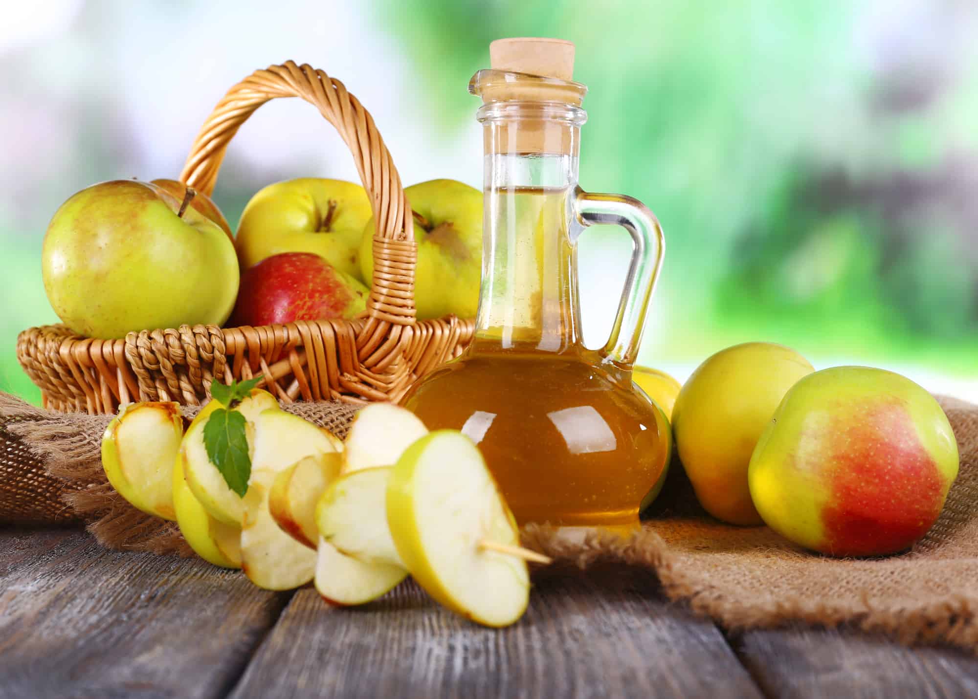 Apple cider vinegar in glass bottle and ripe fresh apples, on wooden table, on nature background