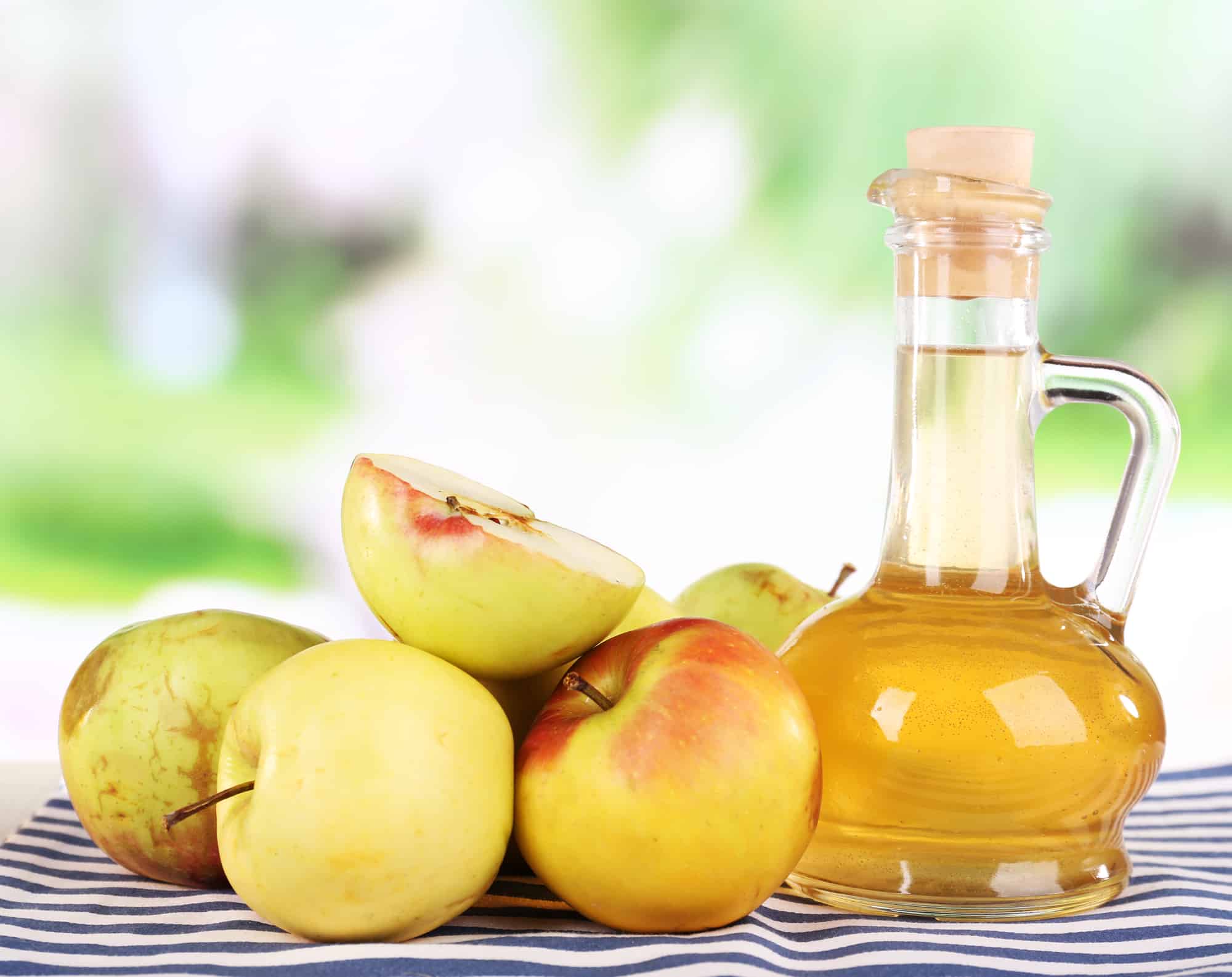 Apple cider vinegar in glass bottle and ripe fresh apples, on wooden table, on nature background