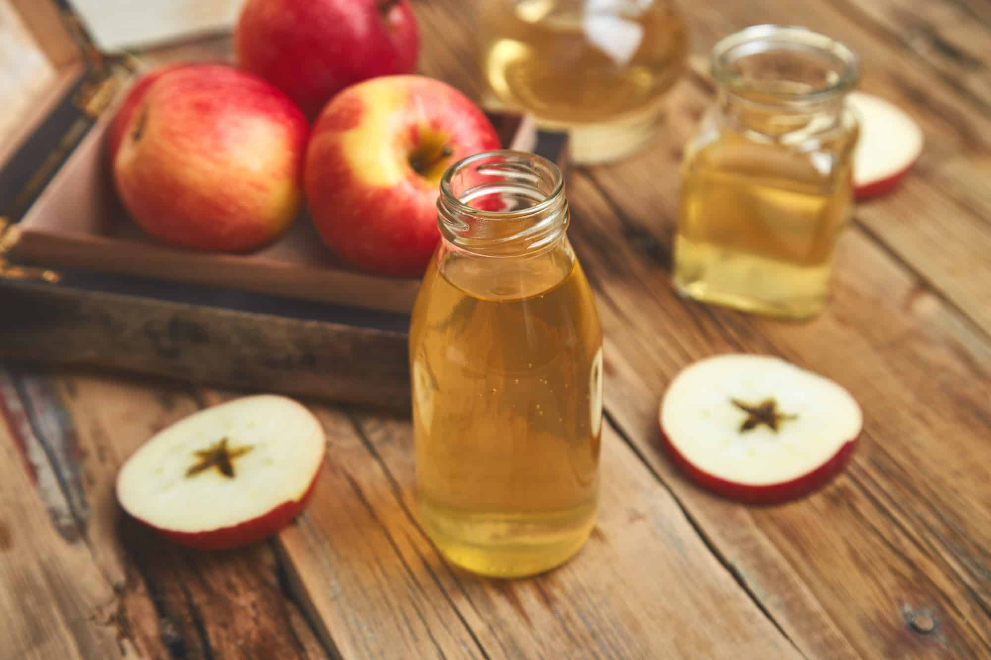 Apple cider vinegar. Glass Bottle of apple organic vinegar on wooden table. Healthy organic drink food. Bottle of fresh cider near autumn red apples. Rustic background