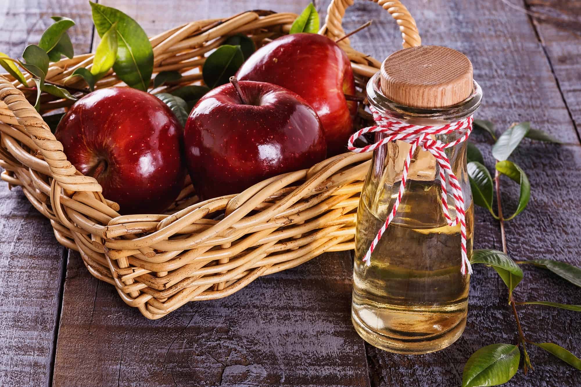 Apple cider vinegar and red apples over rustic wooden background