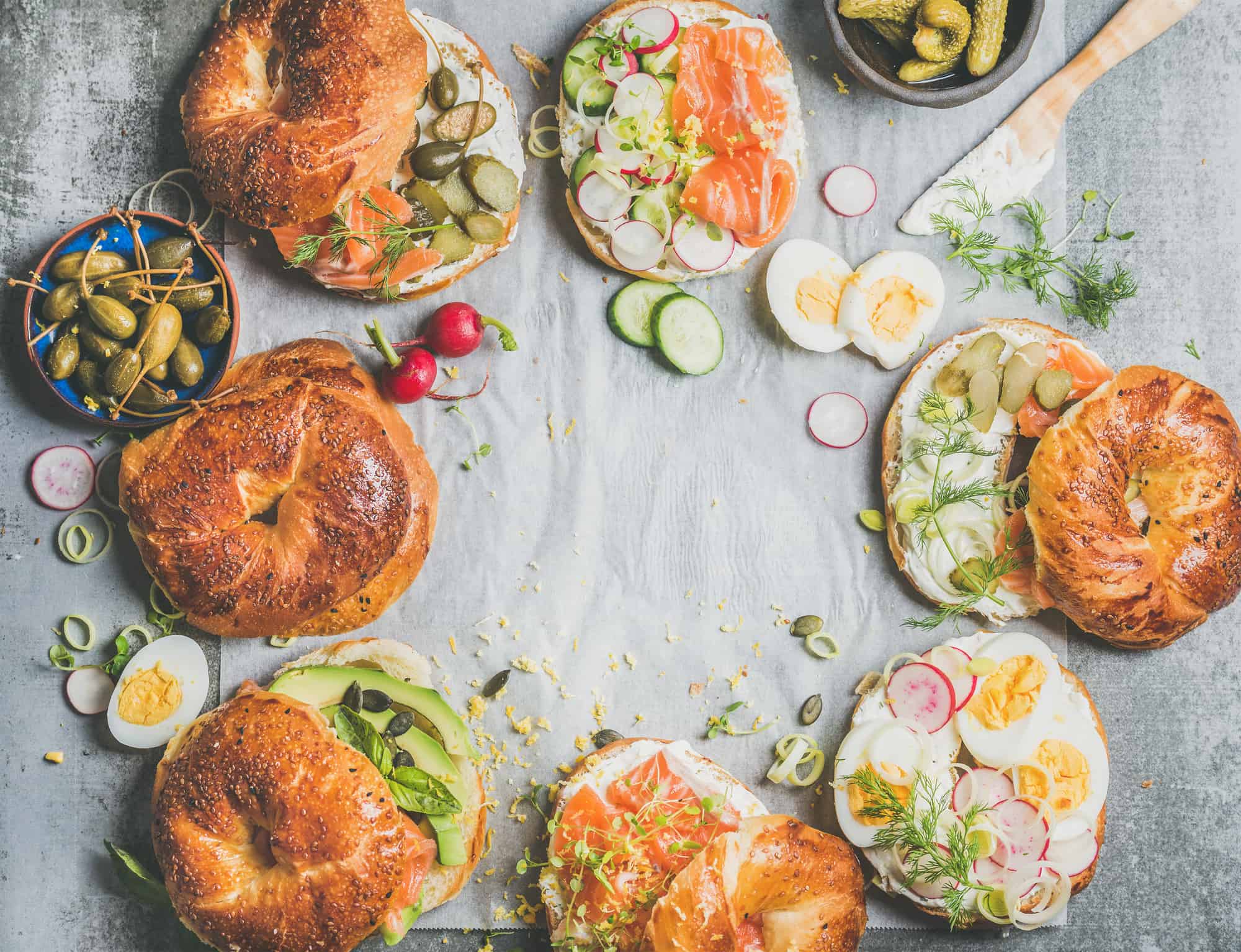 Variety of bagels with salmon, eggs, radish, avocado, cucumber, greens and cream cheese