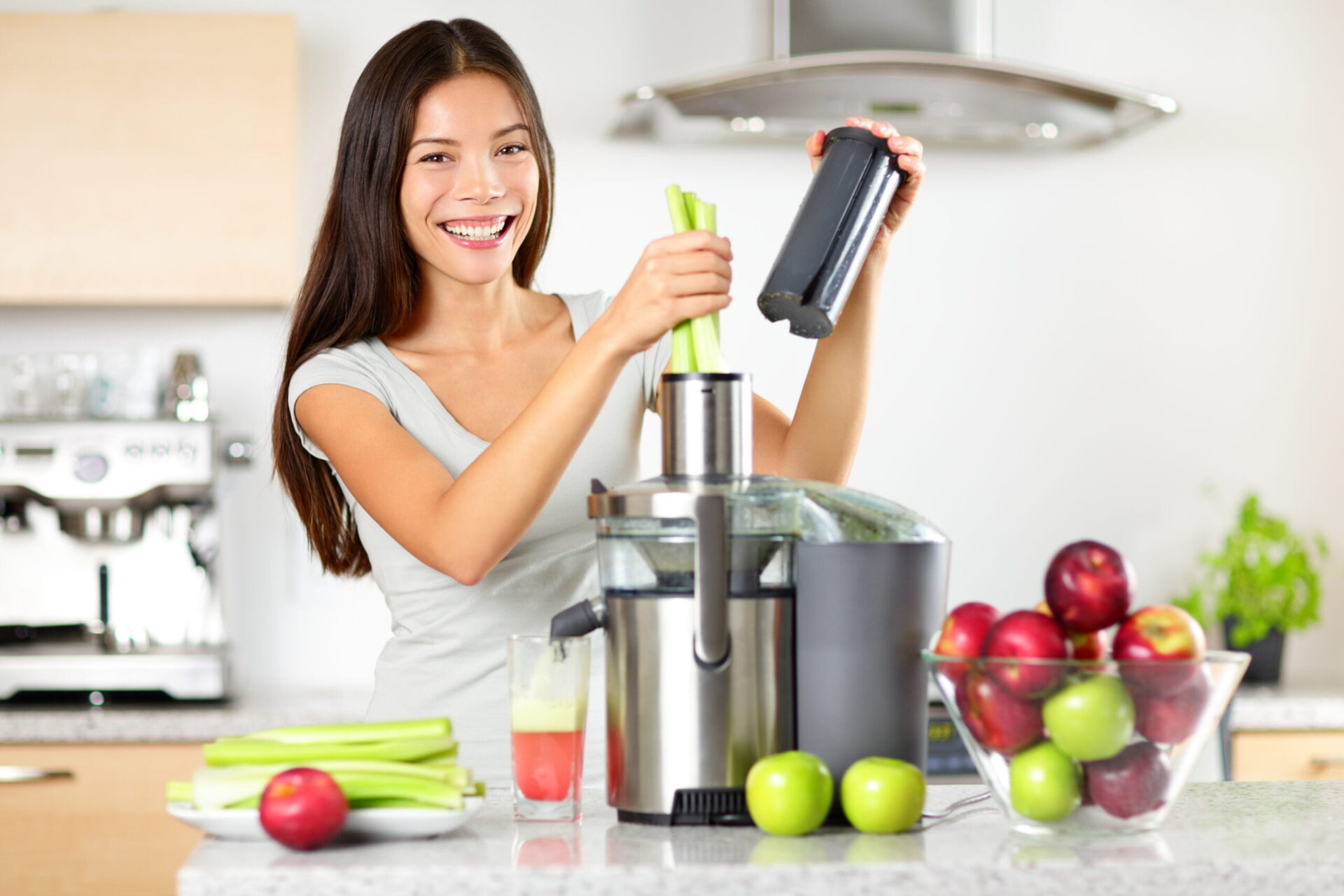 Vegetable juice raw food - healthy eating woman with juicer juicing green vegetables and apple fruits as part of her wellness food. Beautiful happy mixed Asian woman with juice maker in kitchen.