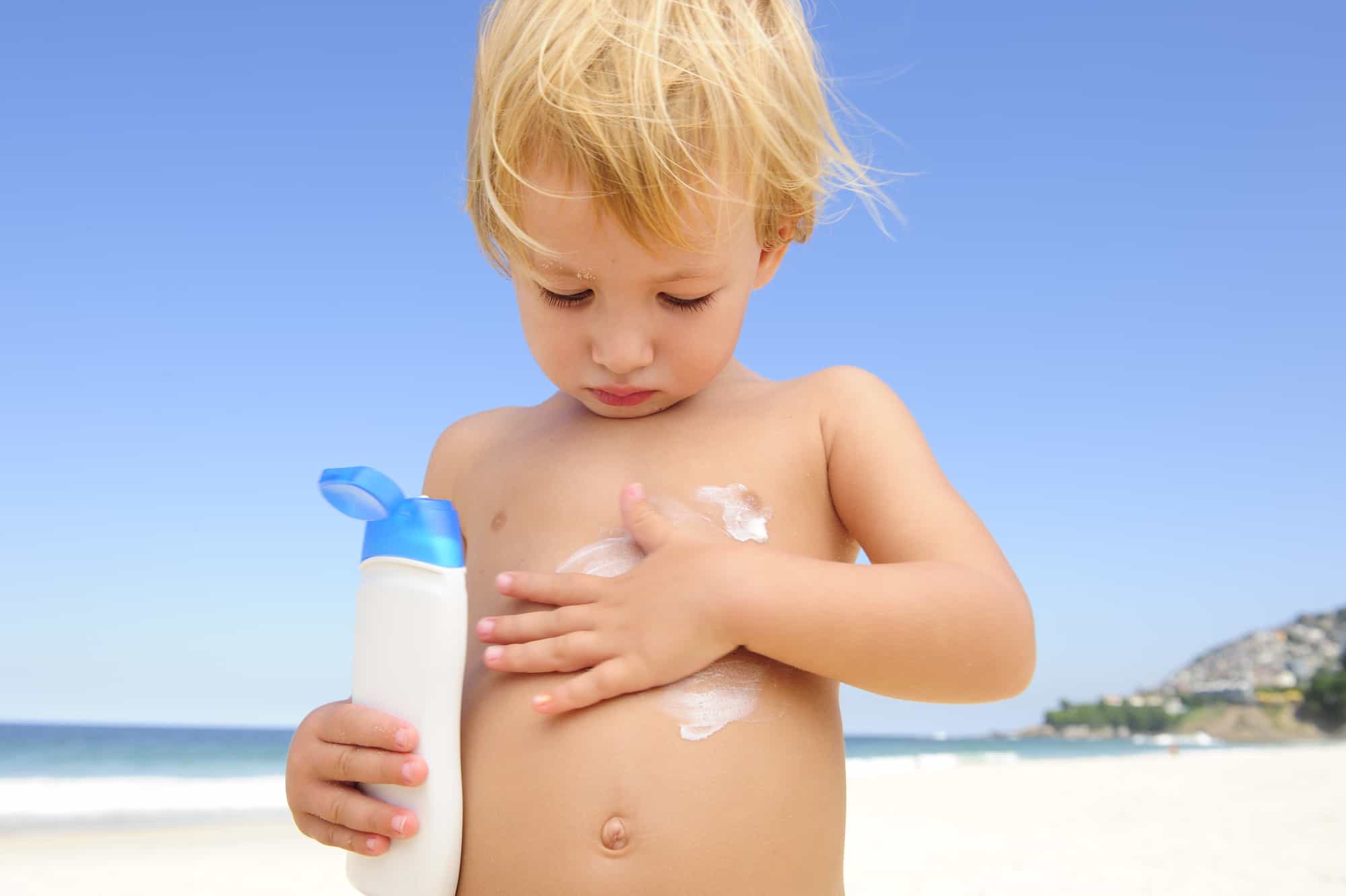 cute child applying oxybenzone sunscreen at the beach