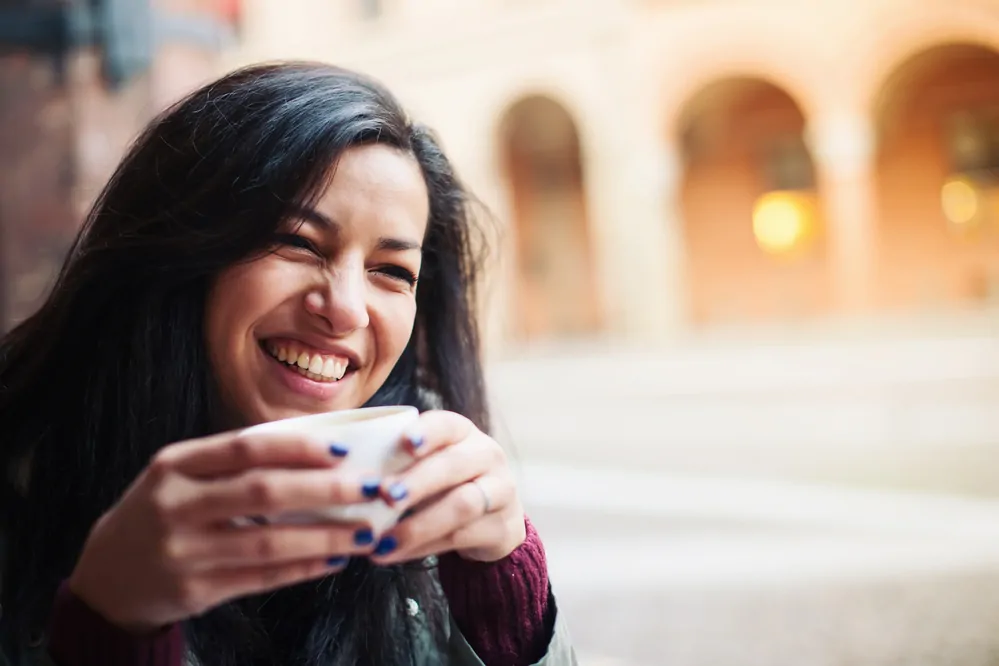 Smiling woman drinking tea in a cafe outdoors