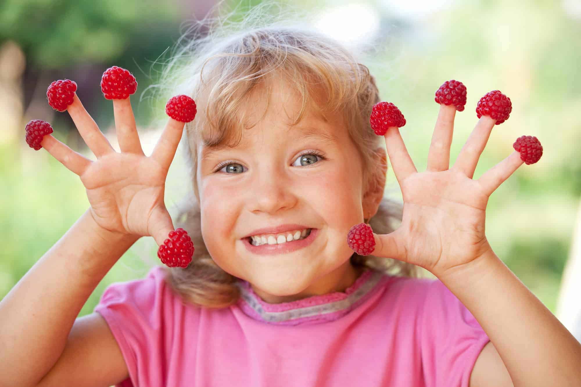 Happy little child with raspberry outdoors