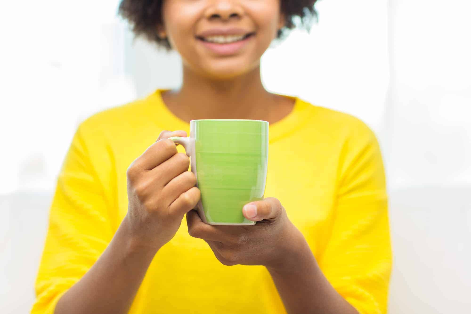 black woman holding a cup of tea in a green mug