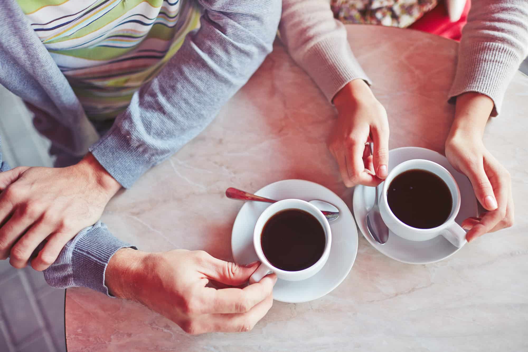 Close up of table and hands of young couple enjoying a cup of coffee at sidewalk restaurant