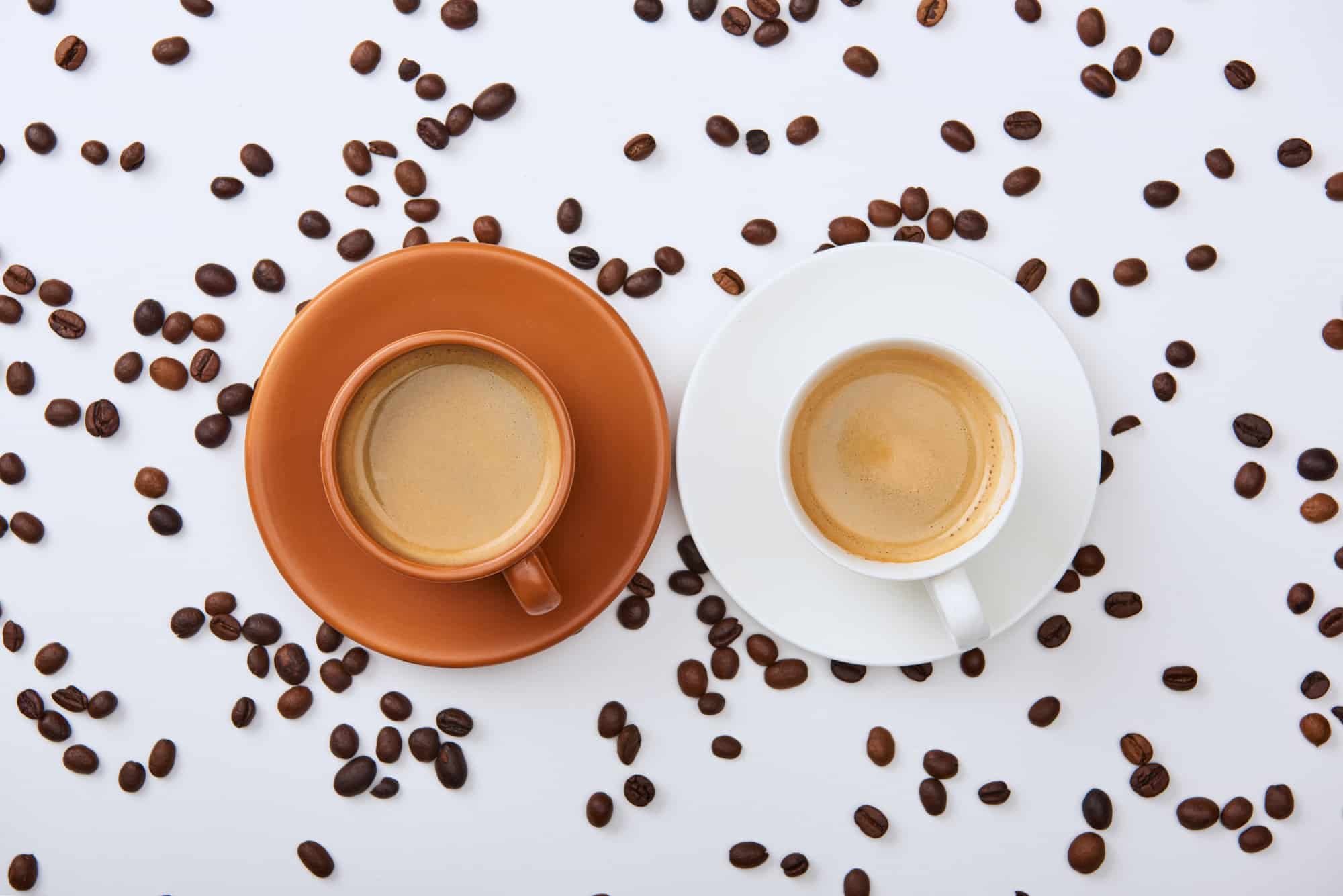 two cups of coffee side by side with cream against coffee beans