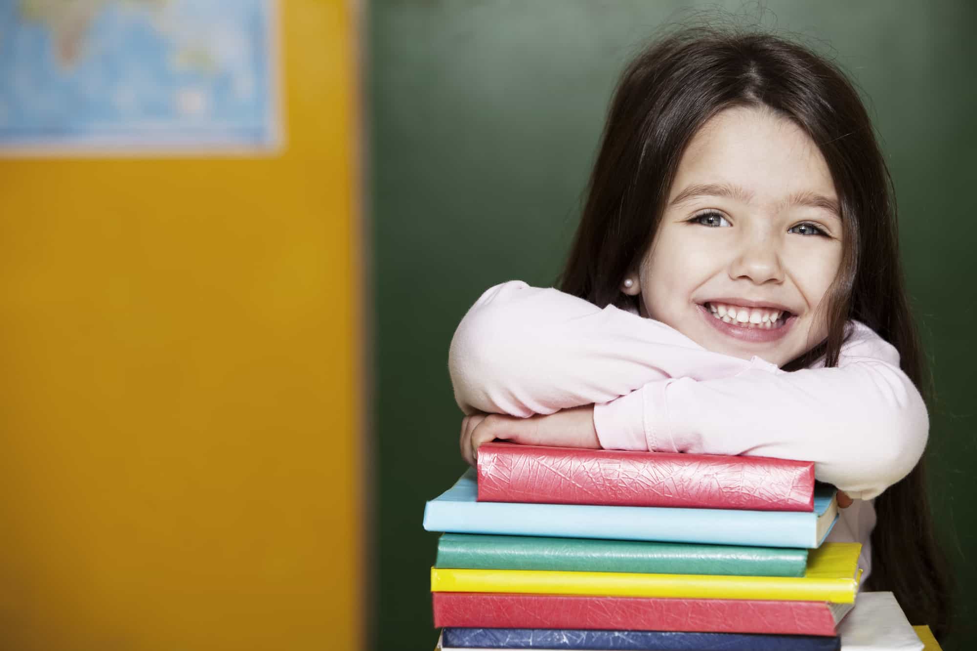 young burnette girl resting on a pile of colorful books smiling