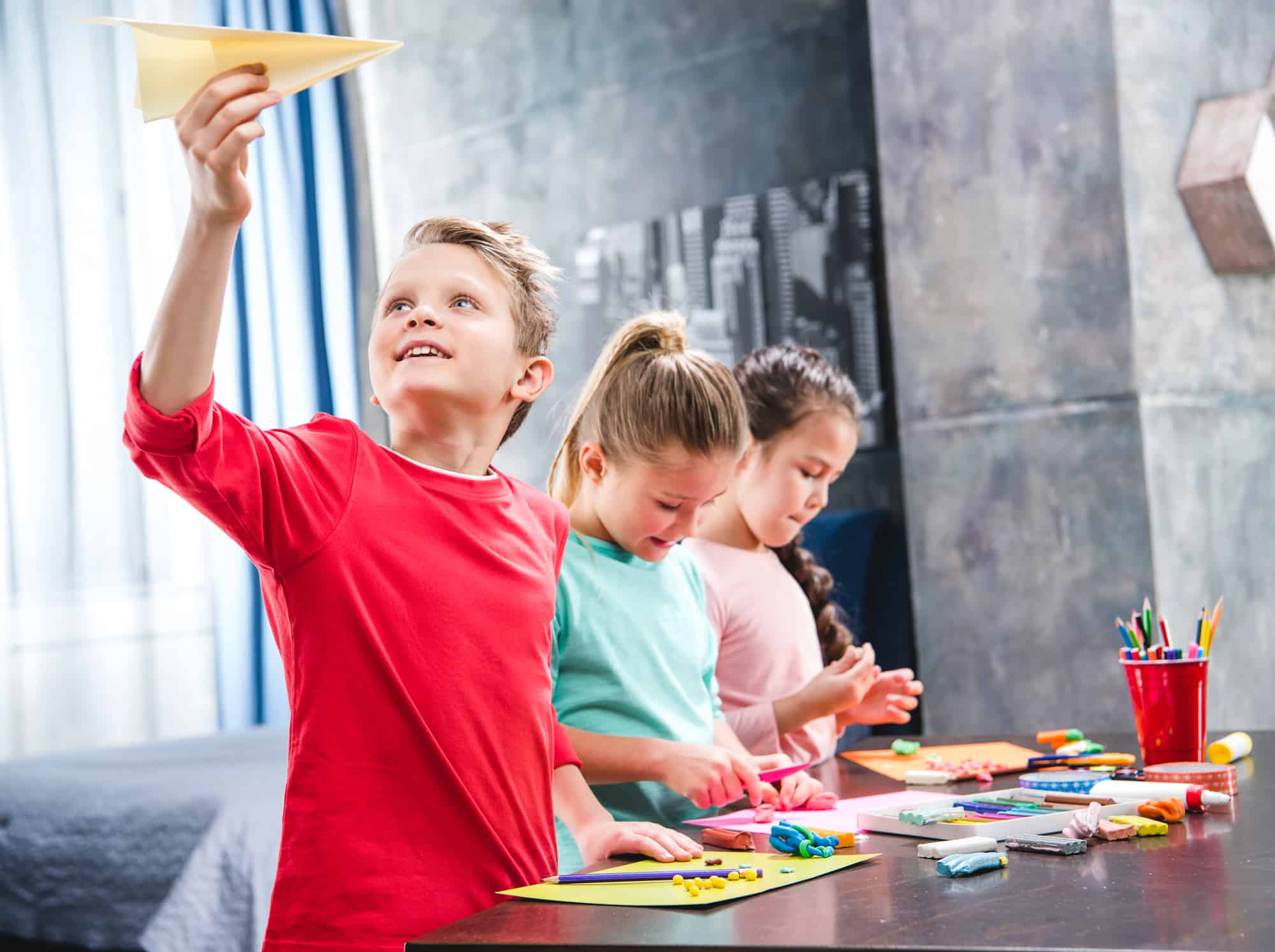 child wearing red shirt holds paper plane