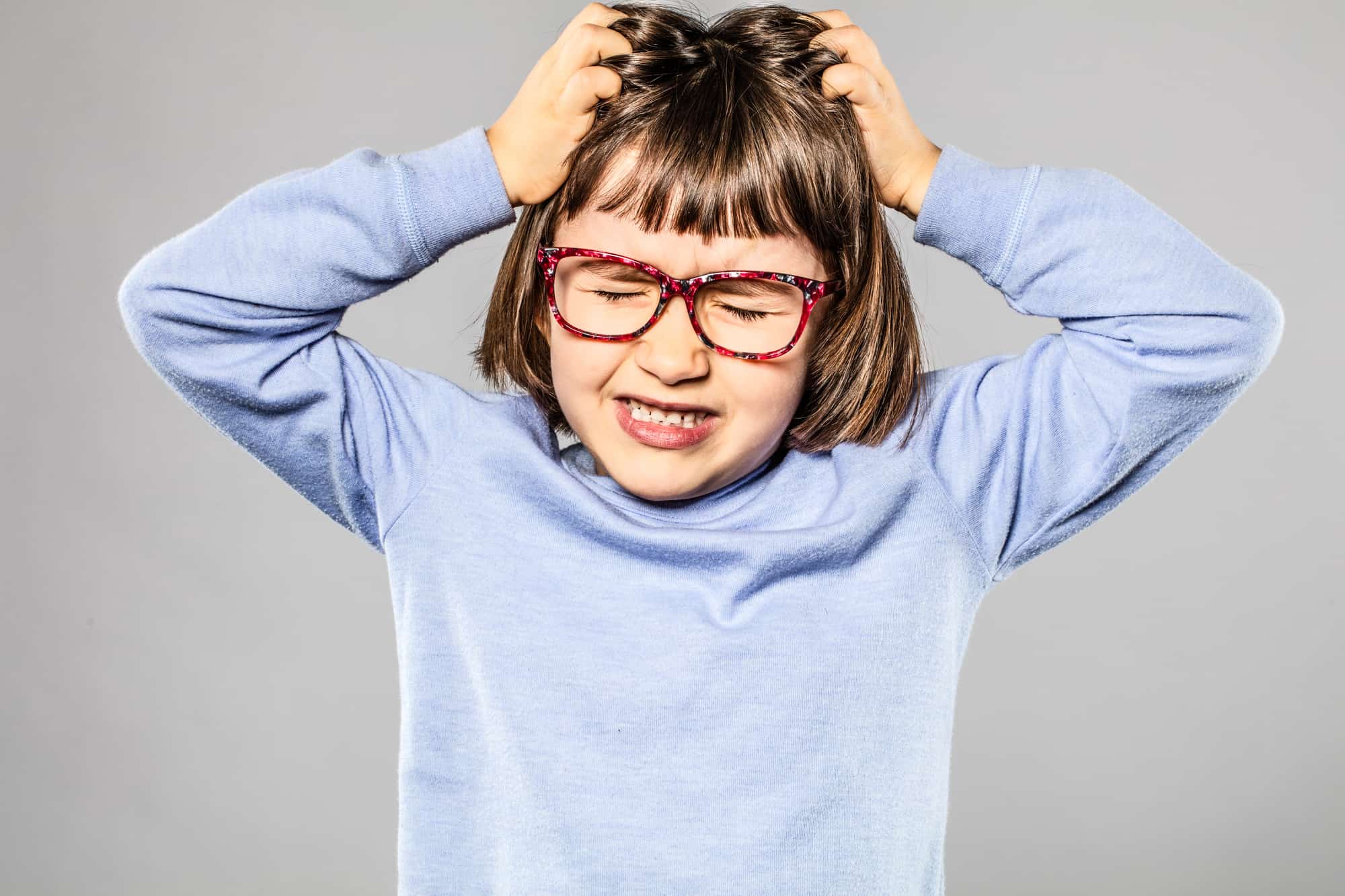 irritated 6-year old young girl with eyeglasses pulling out her hair for itchy allergies or lice or scratching her head 