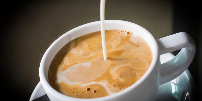 Pouring cream into a cup of coffee