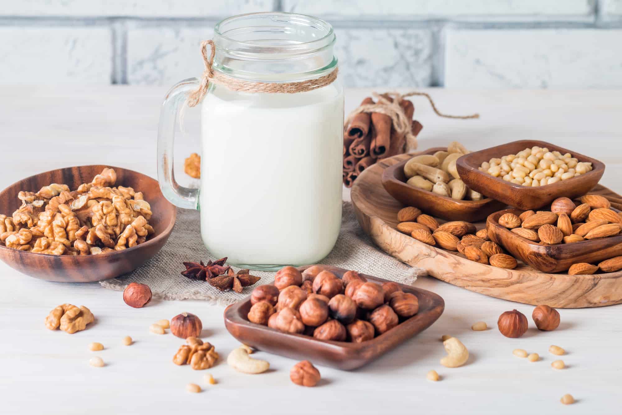 Vegan milk from nuts in glass jar with various nuts on white wooden background
