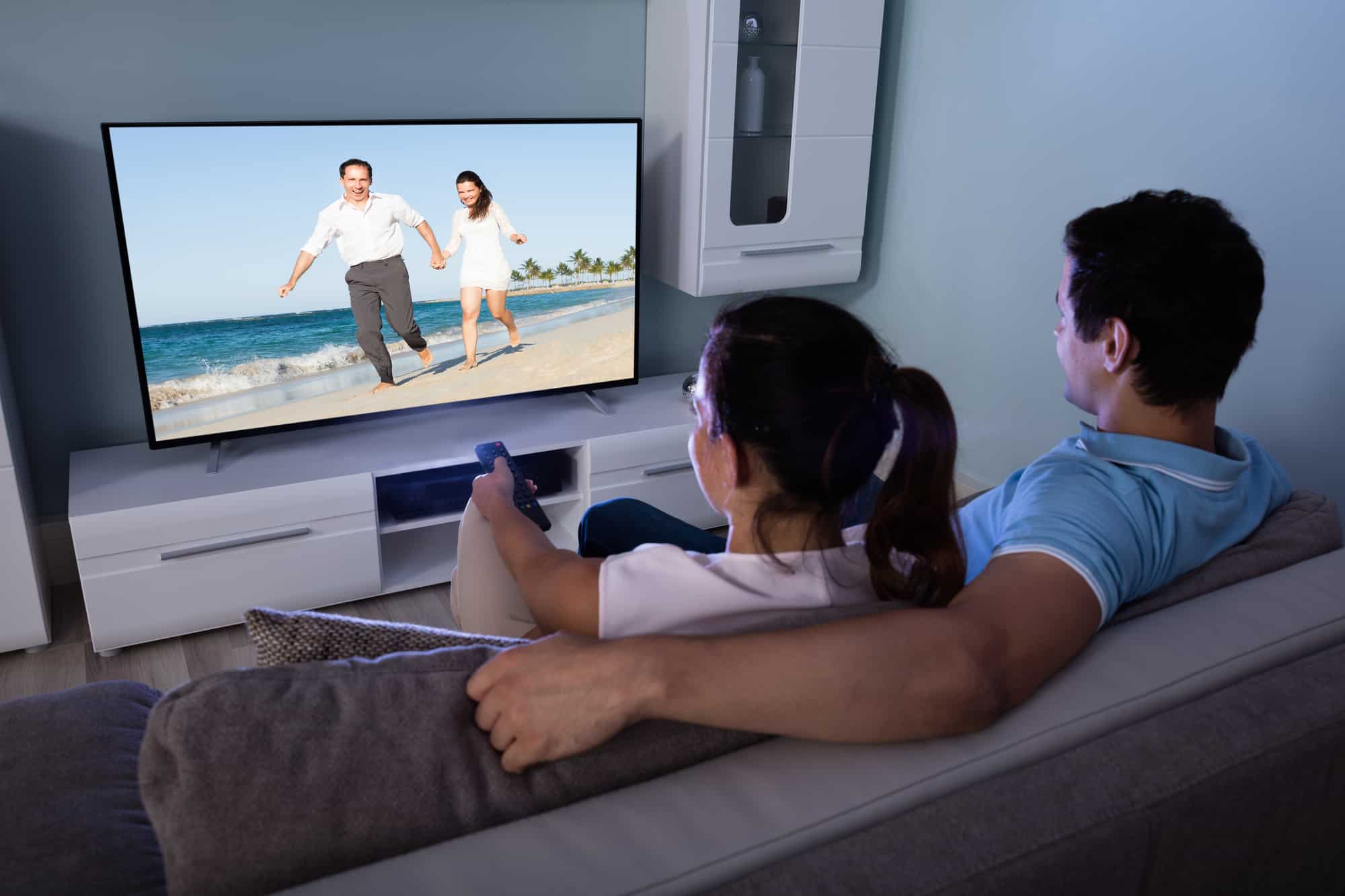 Rear View Of Couple Watching Movie On Television Together In Living Room