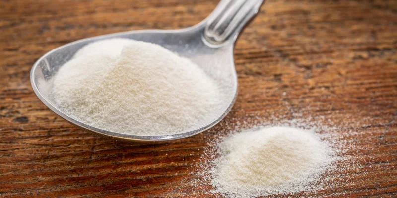 collagen protein powder on a tablespoon against rustic wood