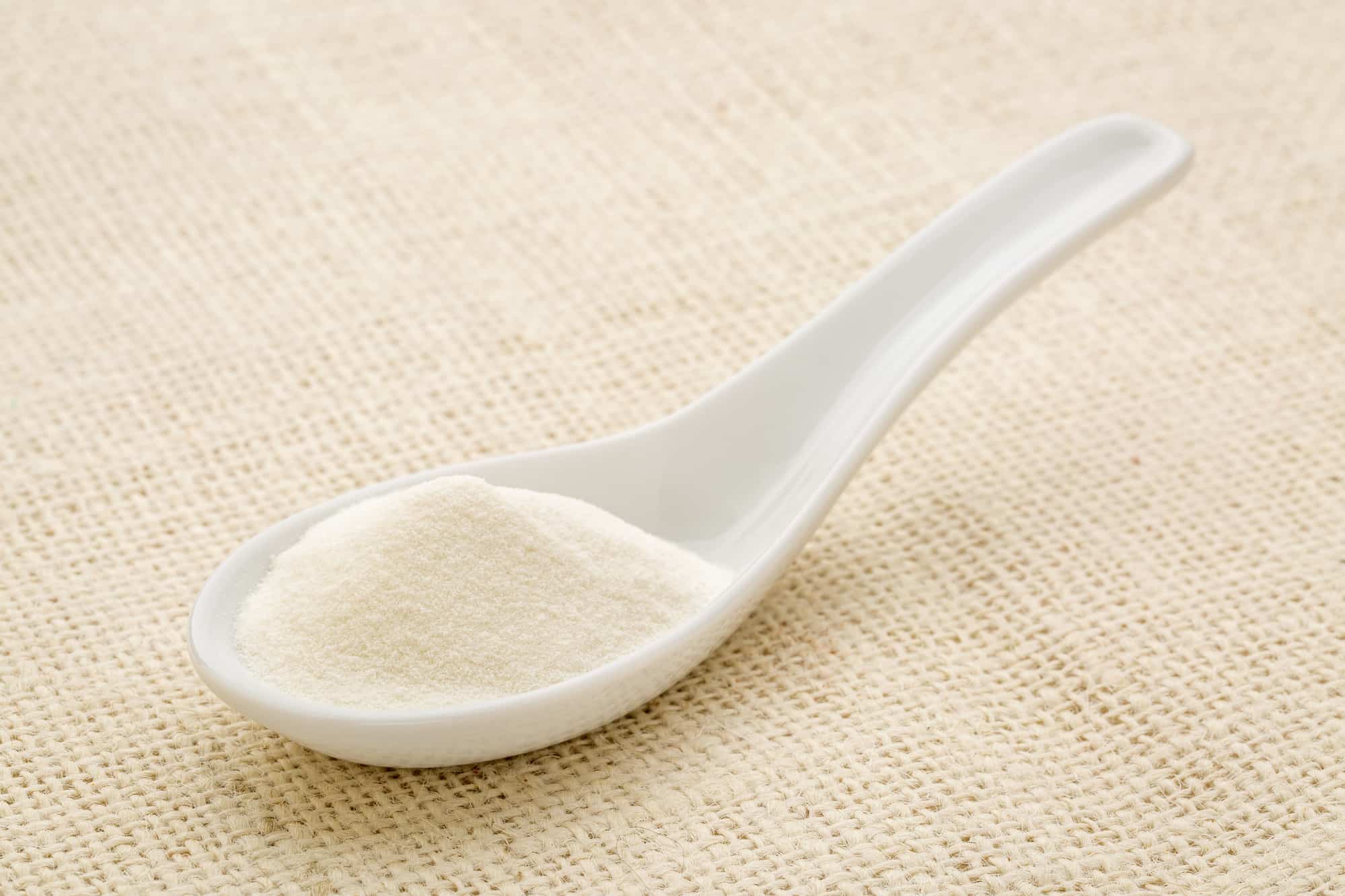 collagen protein powder on a white Chinese spoon against burlap canvas