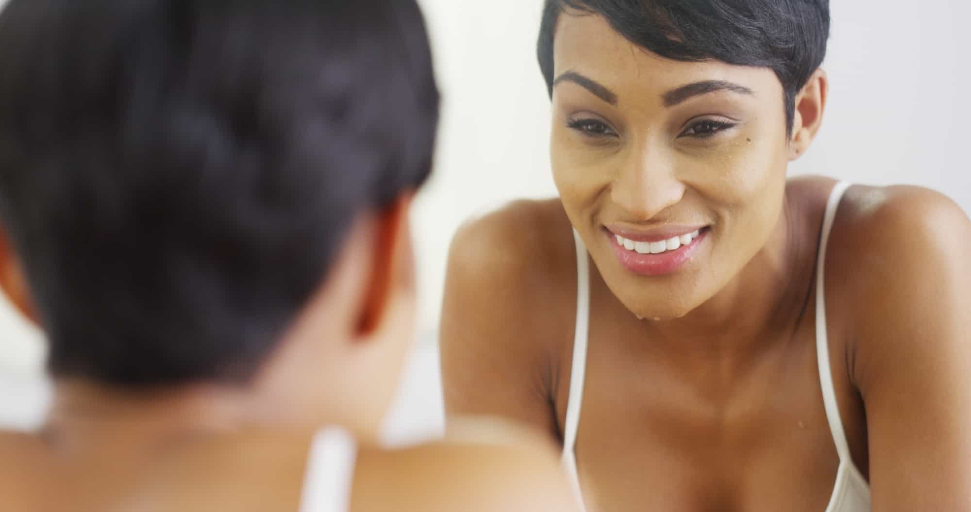 Black woman cleaning face with water and looking in mirror