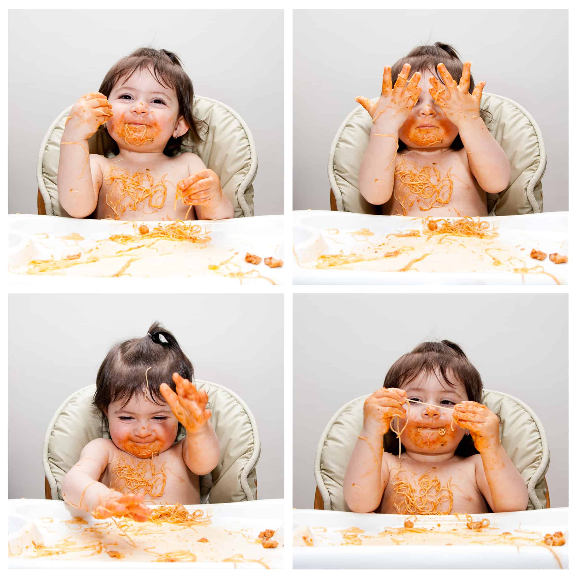Happy baby having fun eating messy showing hands covered in Spaghetti Angel Hair Pasta red marinara tomato sauce.