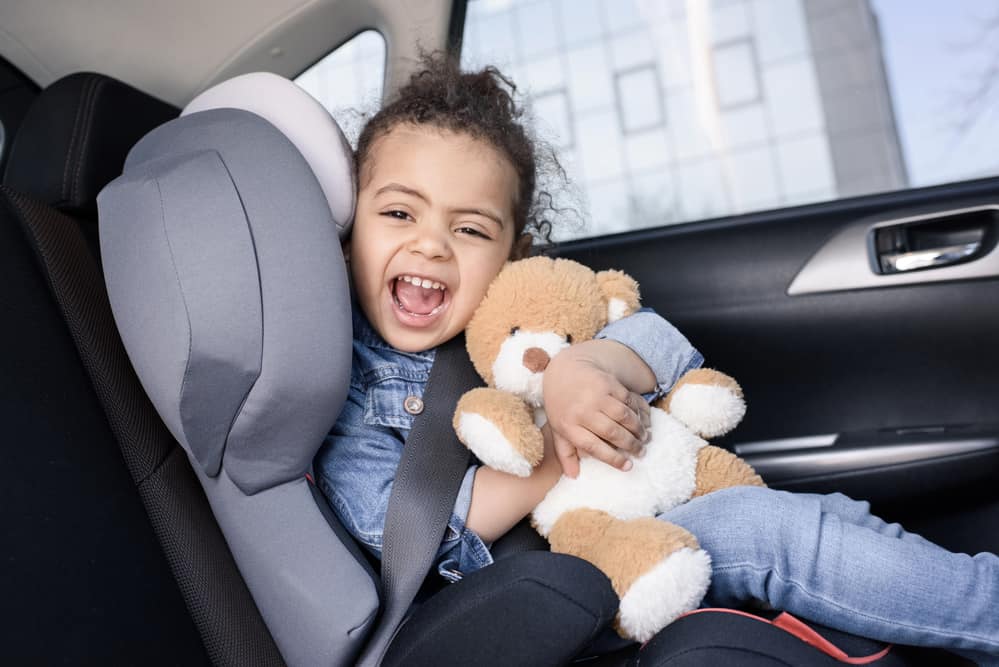 Cute young girl hugging bear in her car seat