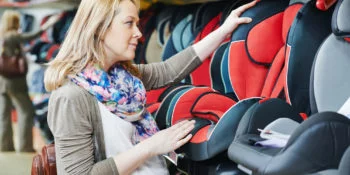 woman choosing child car seat for newborn baby in shop
