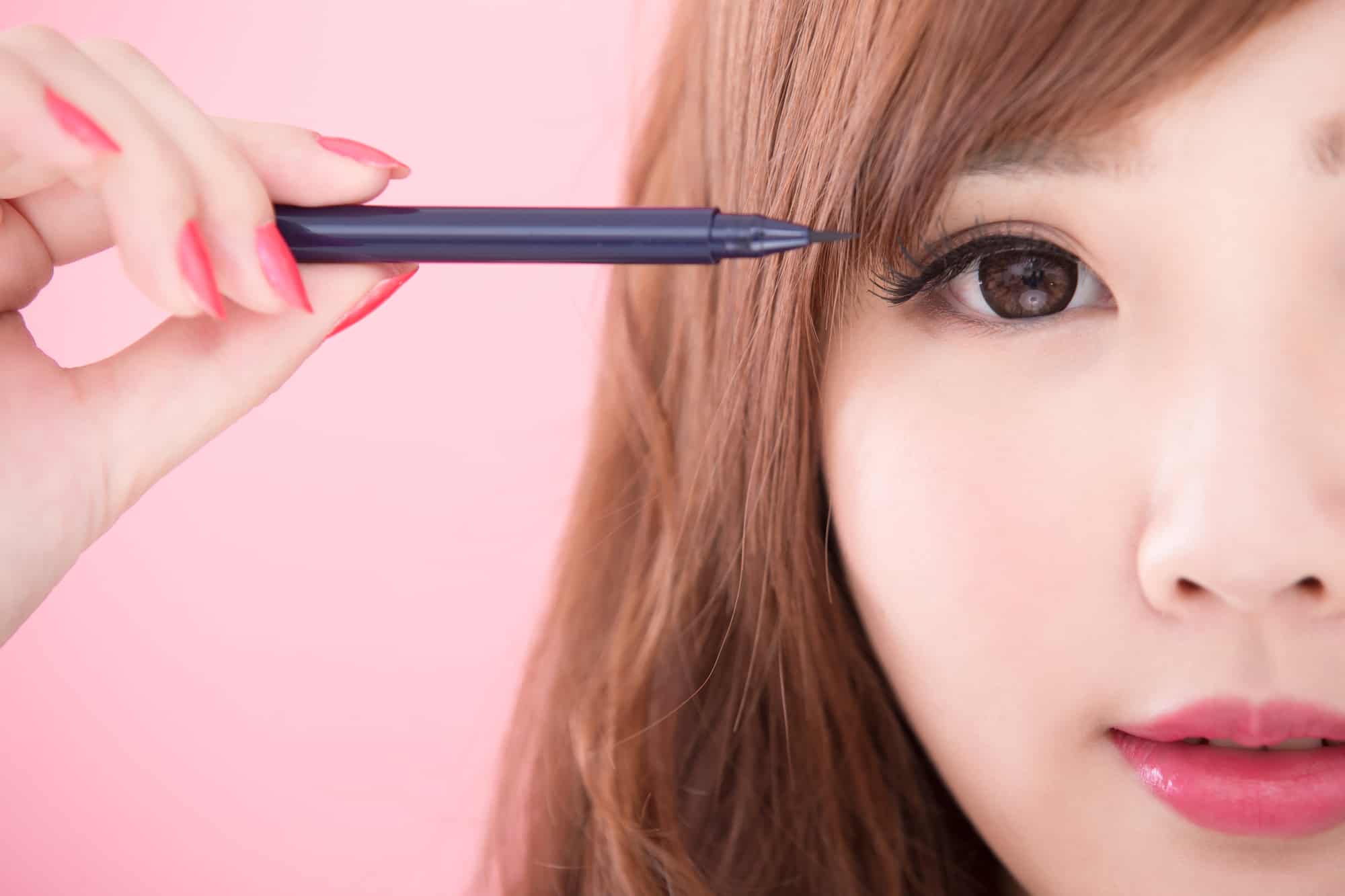 beasian woman puts on eyeliner with pink background