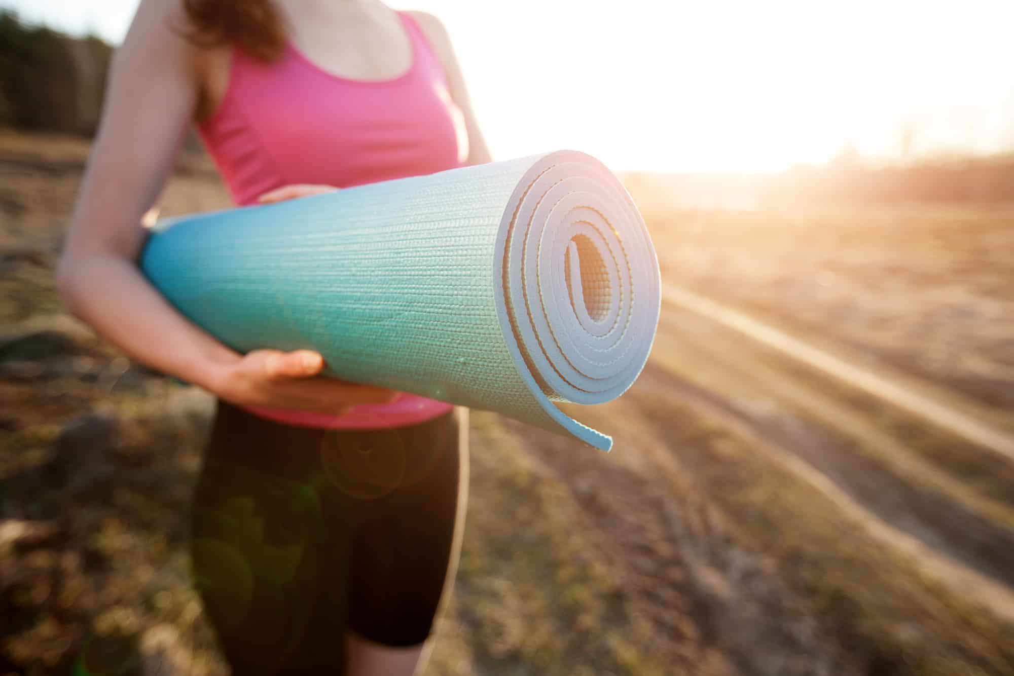 woman walking with a yoga mat outside during sunset n a rural area wearing sports wear and doing yoga