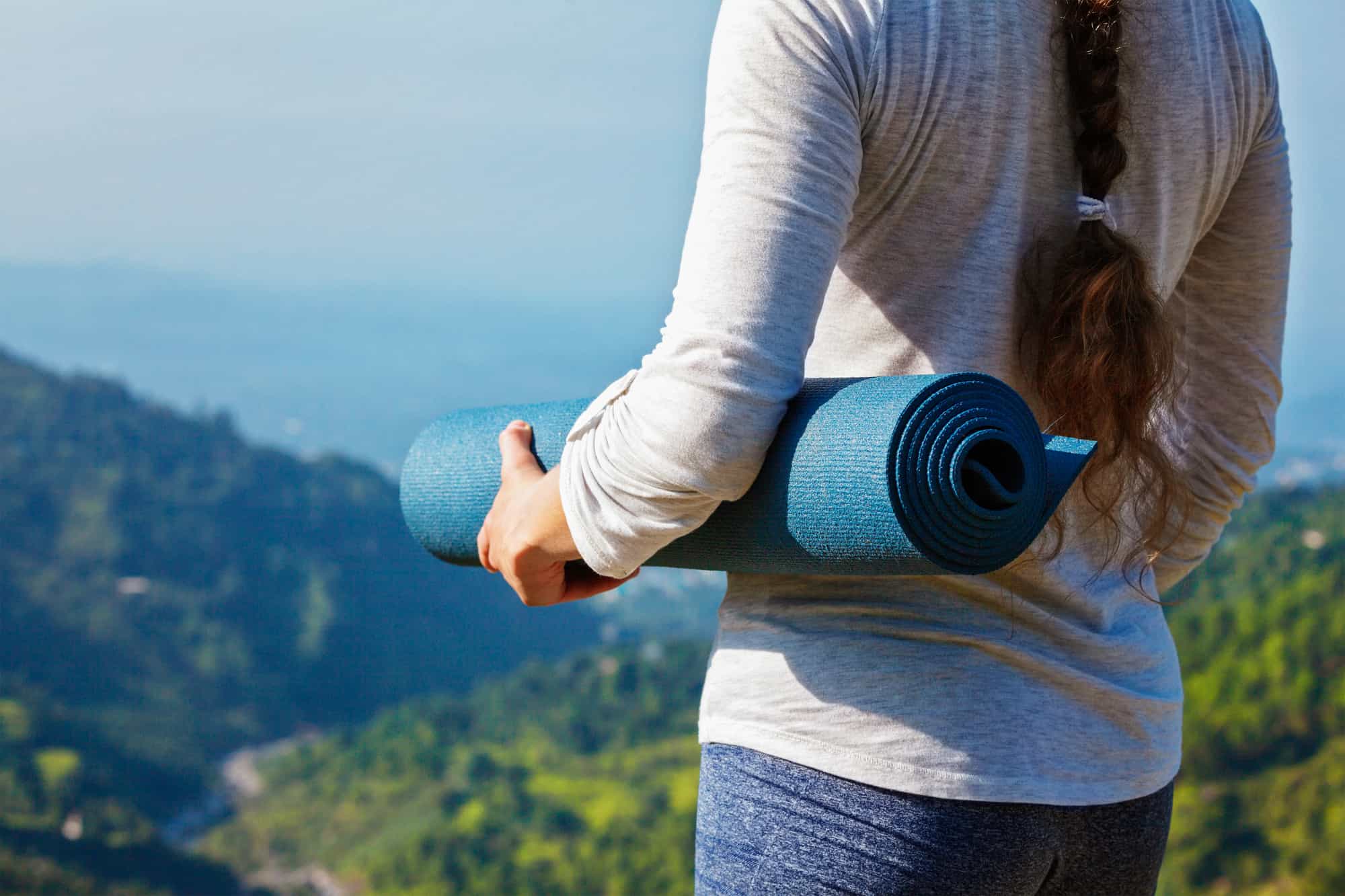 Woman standing with yoga mat outdoors in mountains close up with copyspace getting ready for yoga exercise