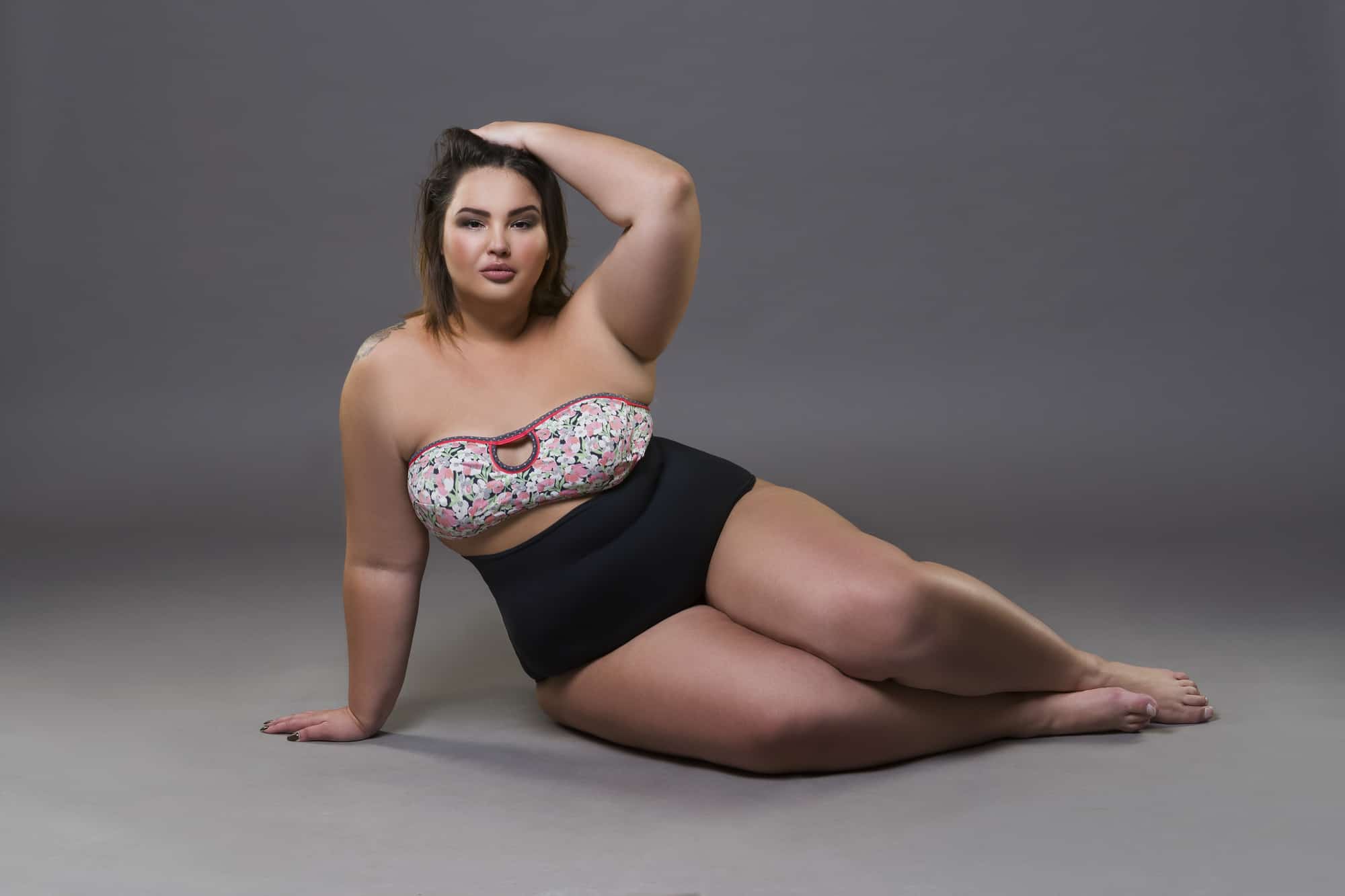 Plus size fashion model in sexy swimsuit, young fat woman on gray studio background, overweight female body, fu