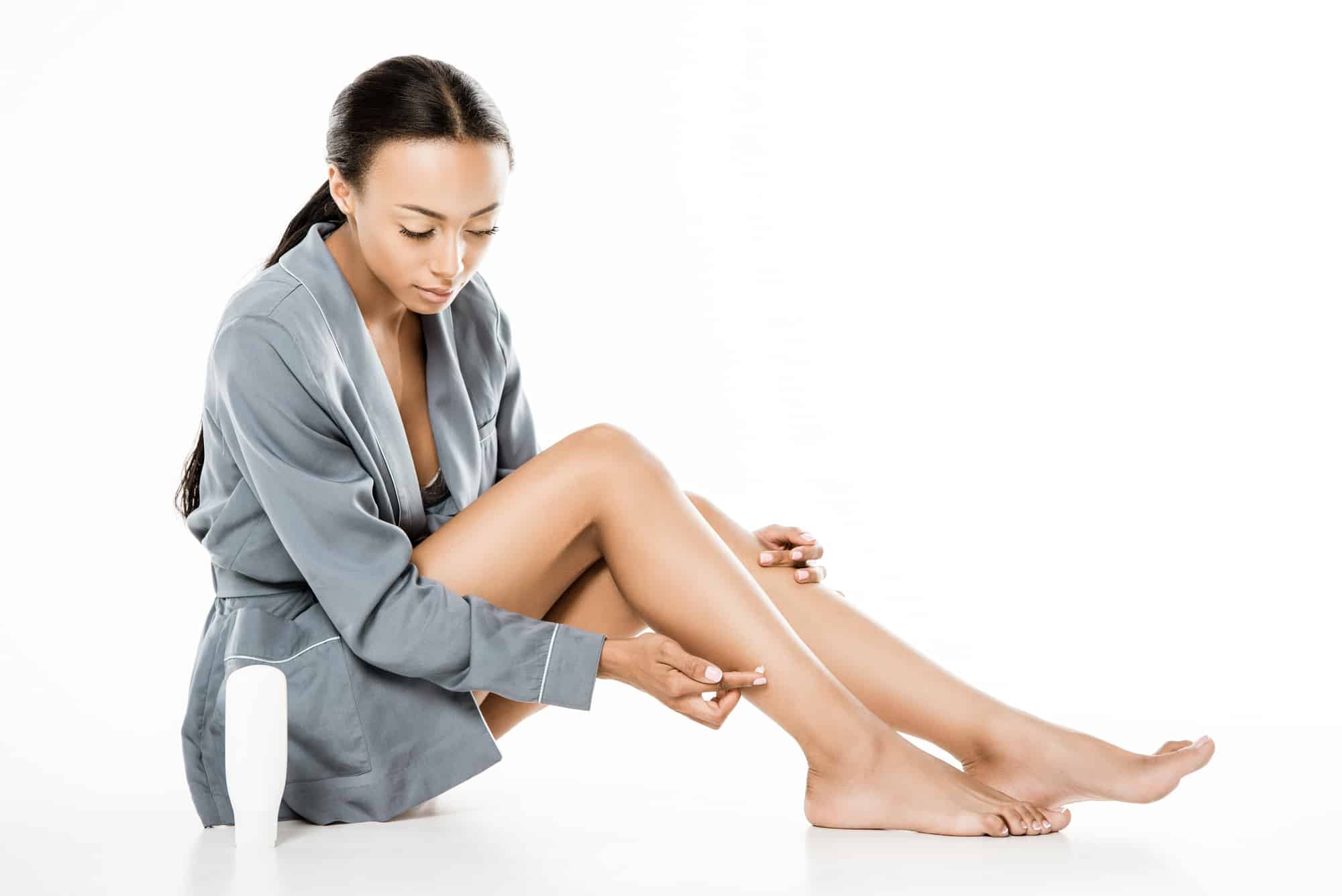 woman of color putting lotion on her dry skin on her legs