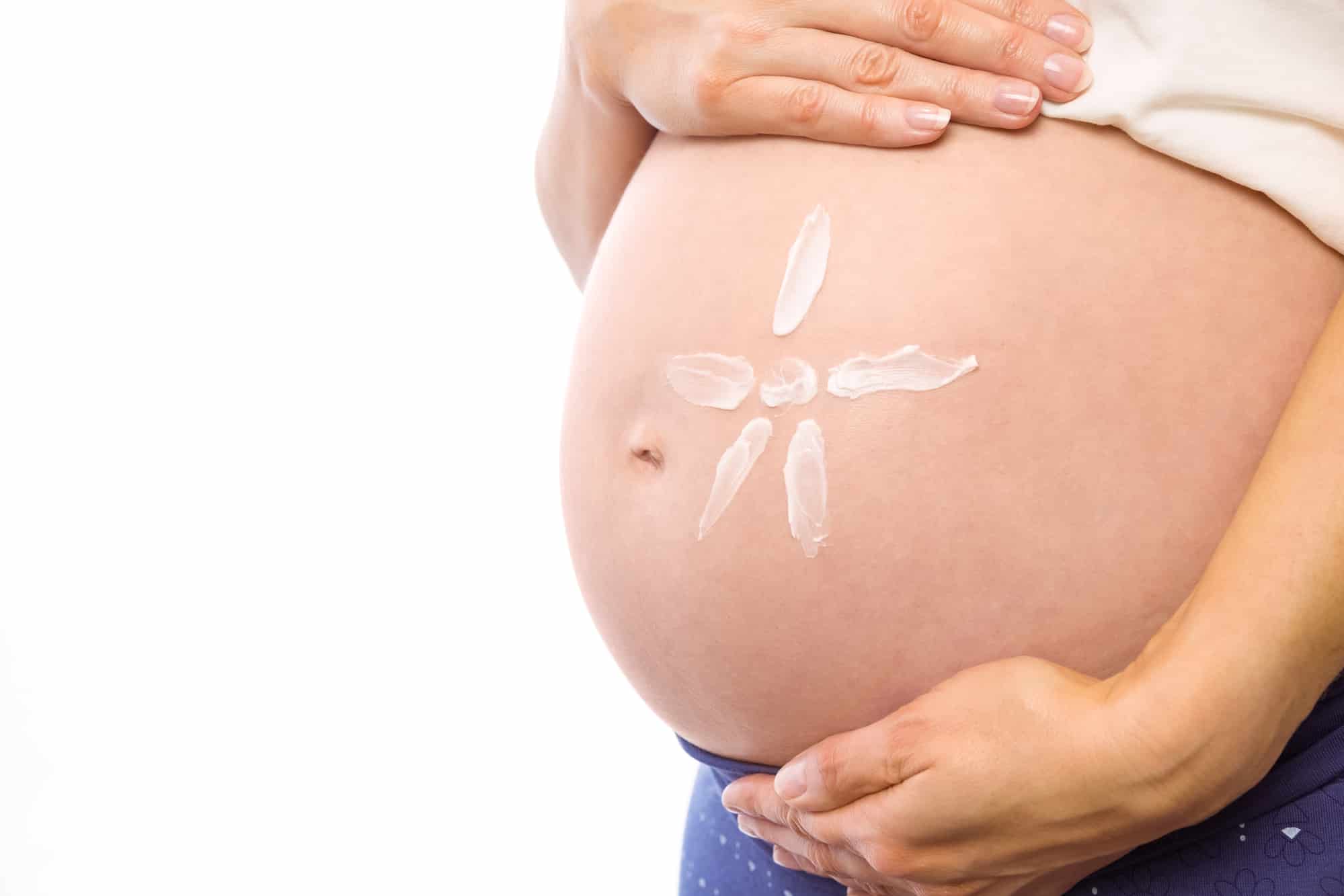 Pregnant woman with cream on bump on white background