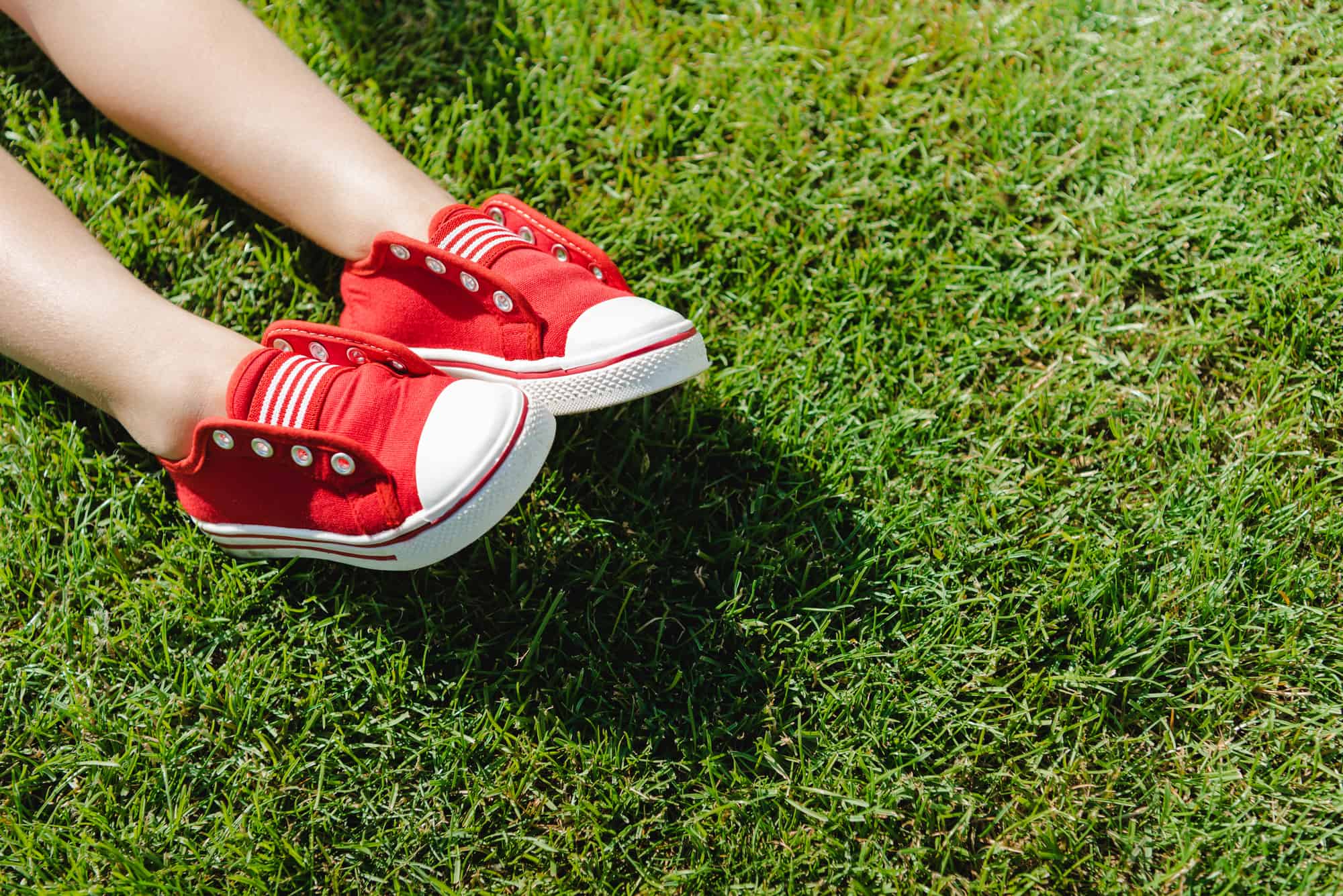 small boy wearing red shoes laying on grass treated as organic land care