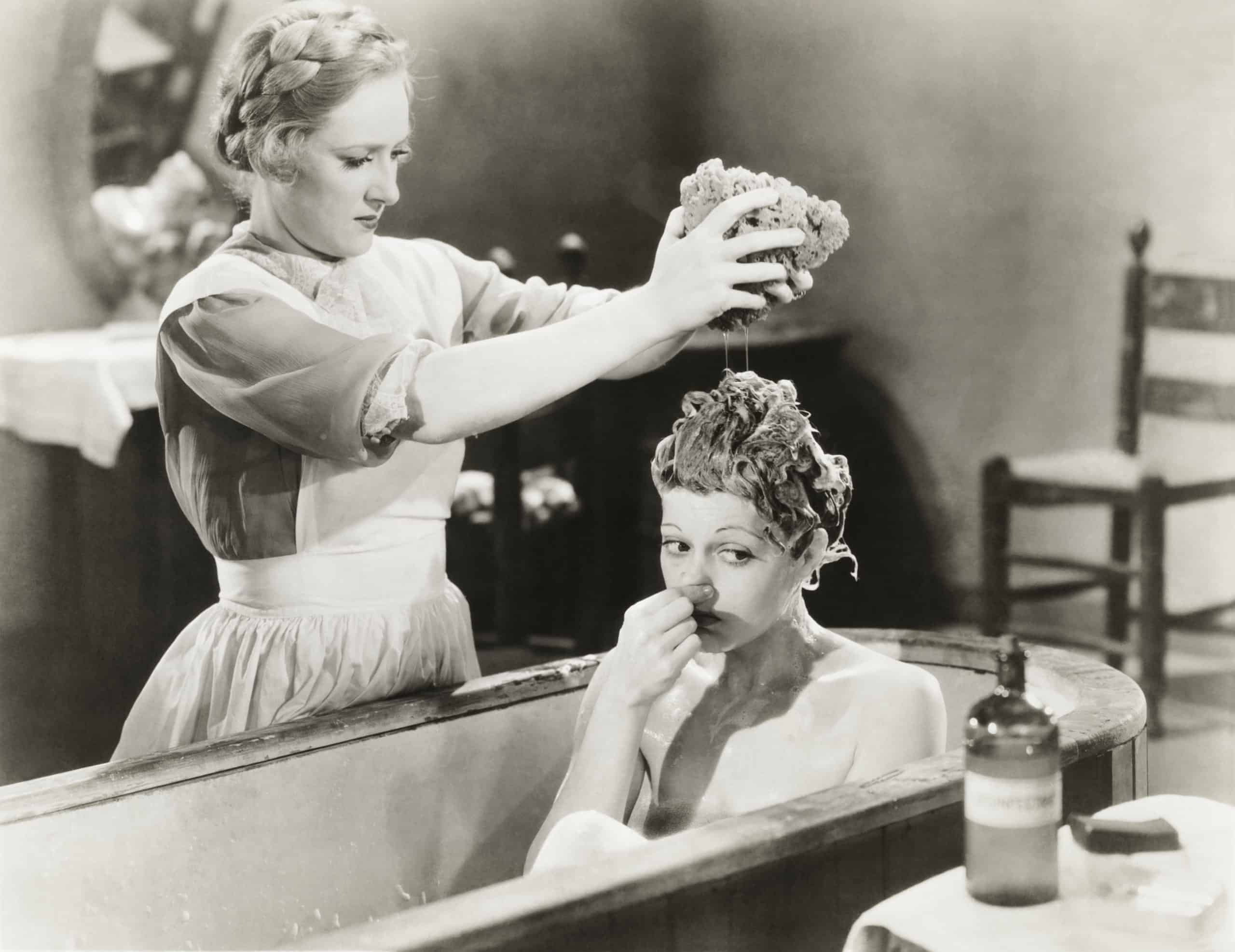 Woman giving other woman bath in tub vintage