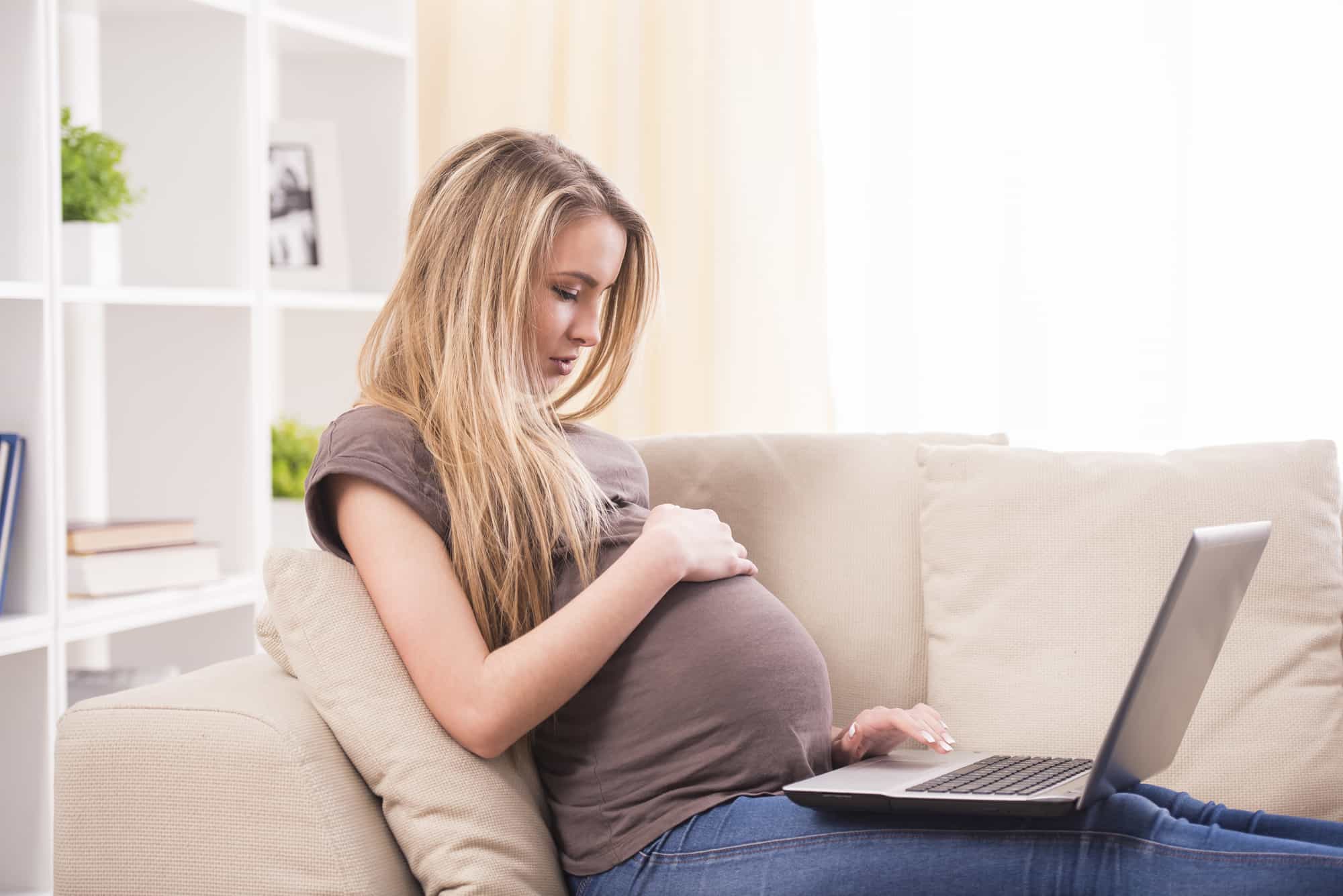 Beautiful pregnant woman working on laptop while lying on a couch