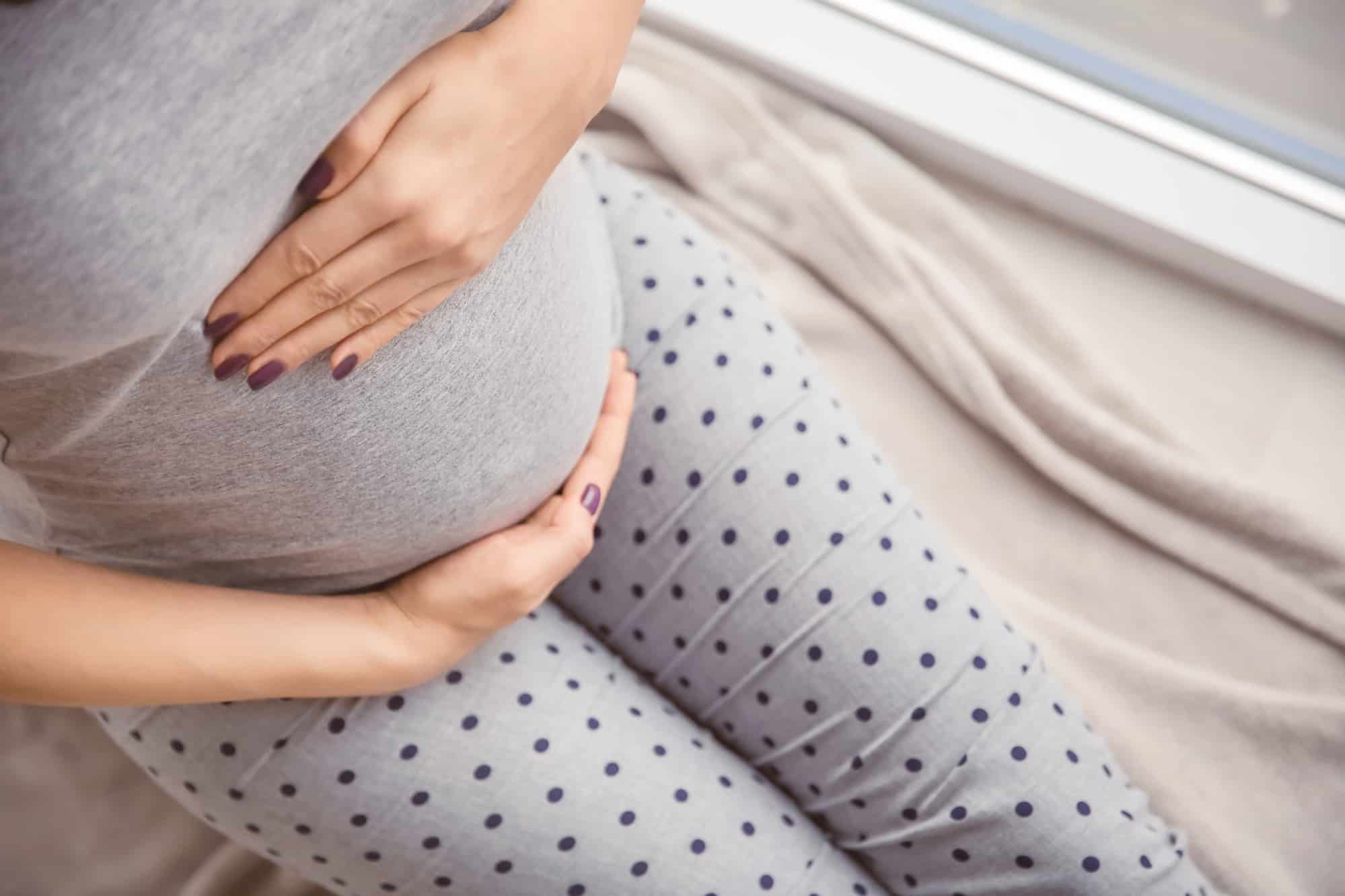 Pregnant woman holding hands on belly indoors