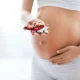 Pregnancy Vitamins And Medications. Close Up Of Pregnant Woman Holding Pills In Hand Near Belly
