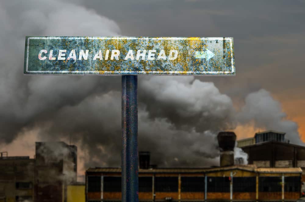 Clean air ahead slogan on the road sign in front of the polluting factory