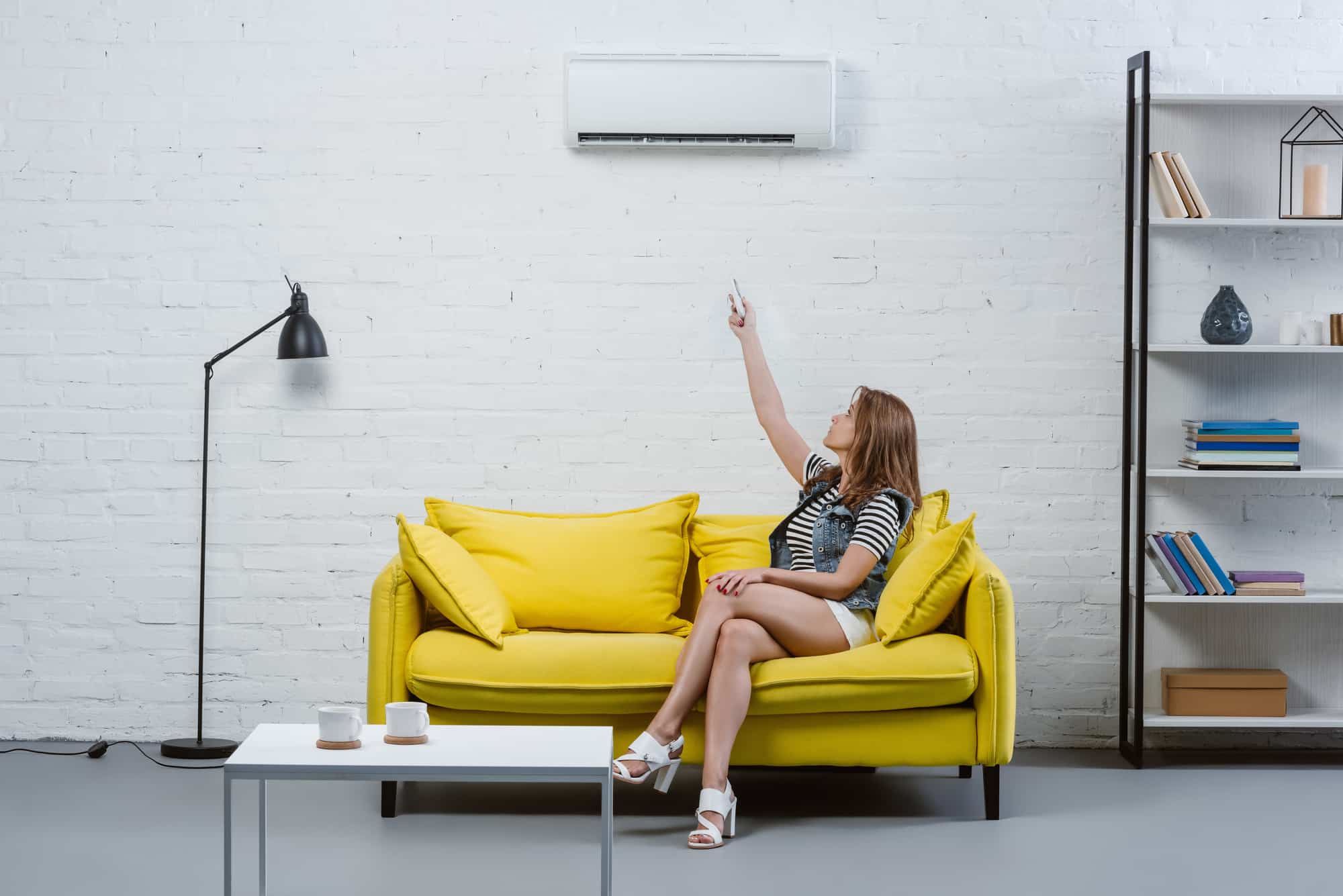 Woman sitting on yellow couch pointing up to her air purifier in a white room