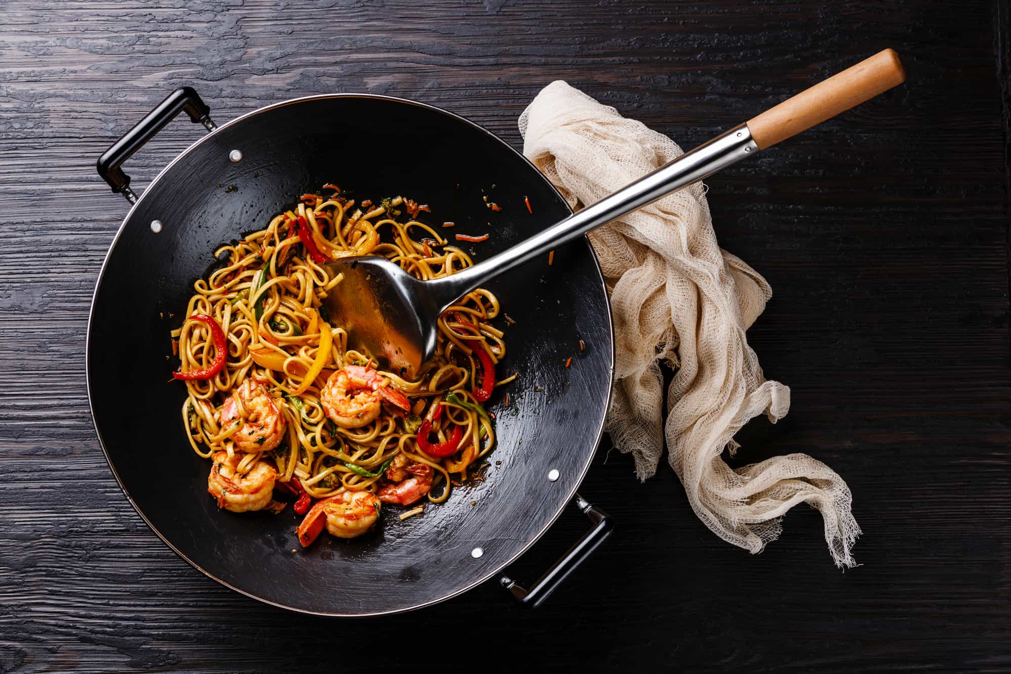 Udon stir fry noodles with prawn shrimp and vegetables in wok pan on black burned wooden background