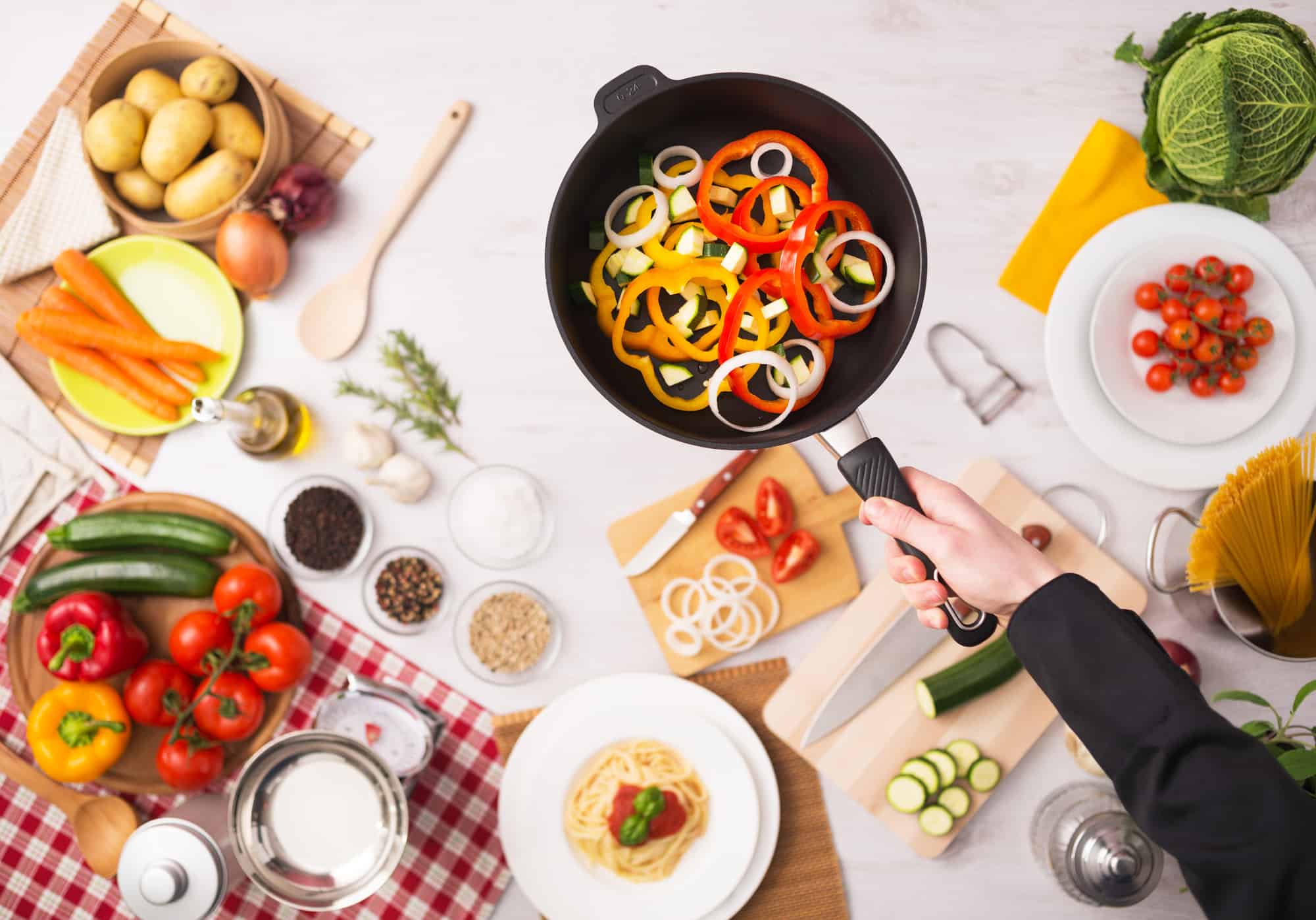 Professional cook frying fresh sliced vegetables in a nonstick pan hands close up, food ingredients and kitchenware on background