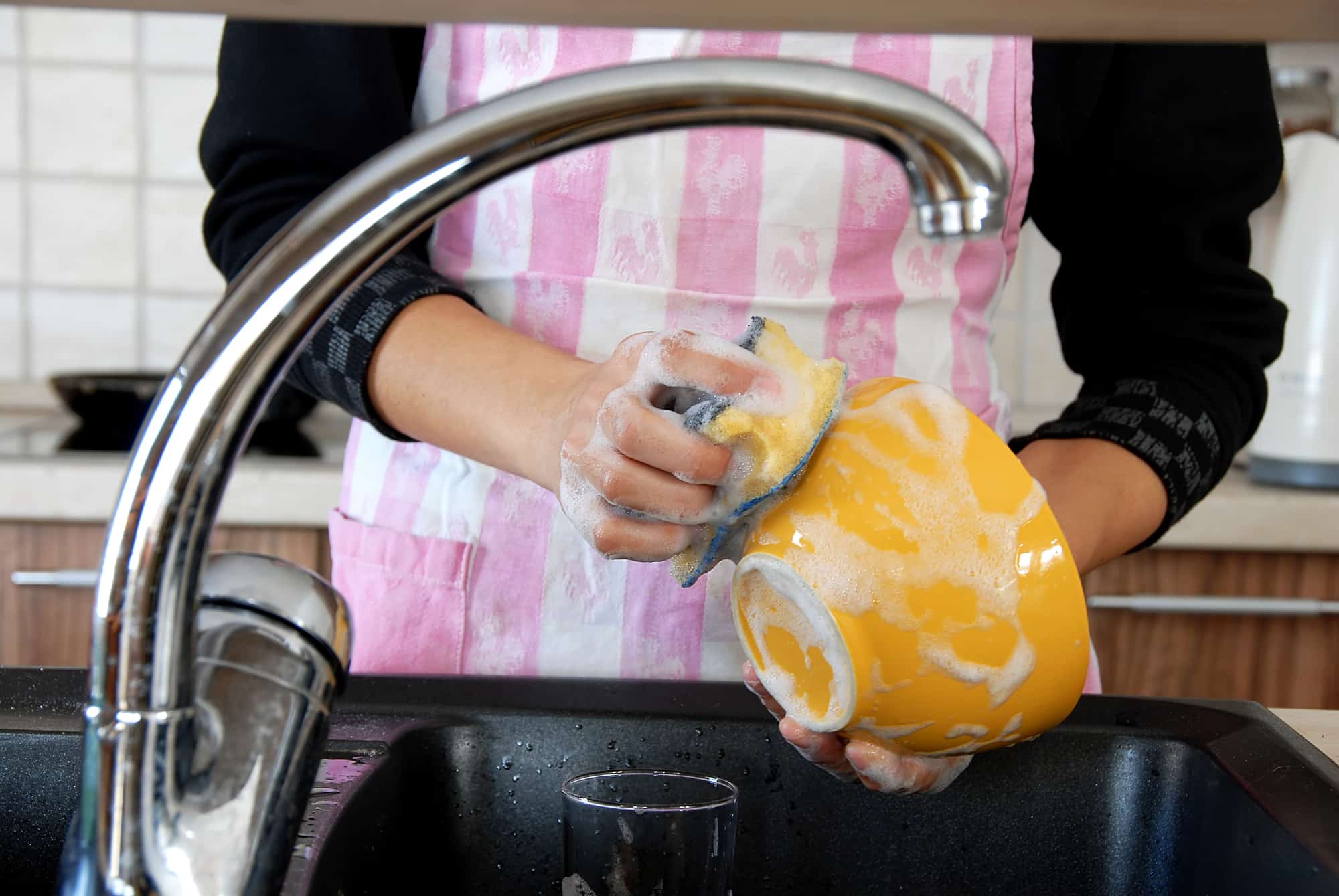 hands with sponge washing dishes in kitchen sink