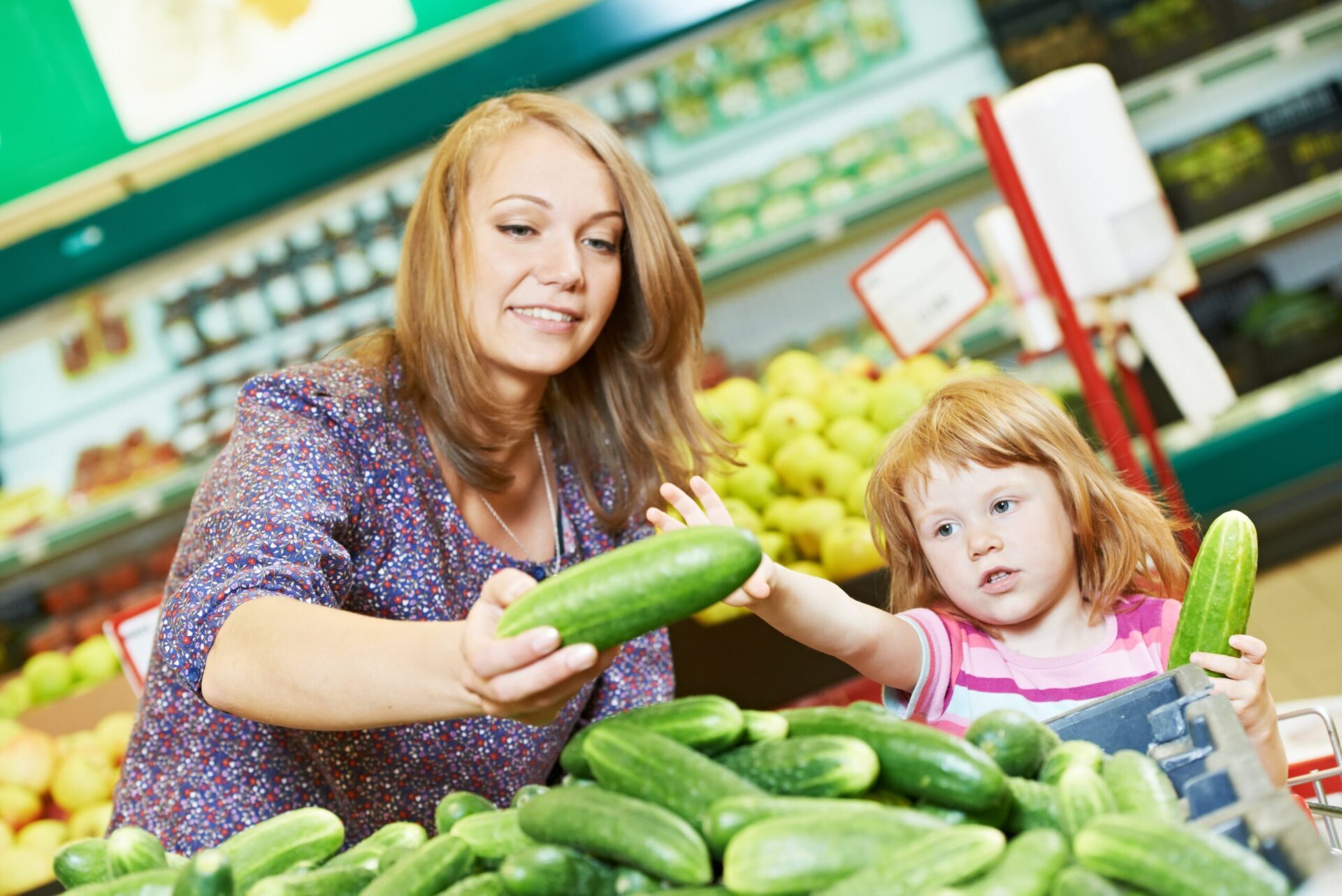 woman and little girl choosing cucumbers during shopping at fruit vegetable supermarket