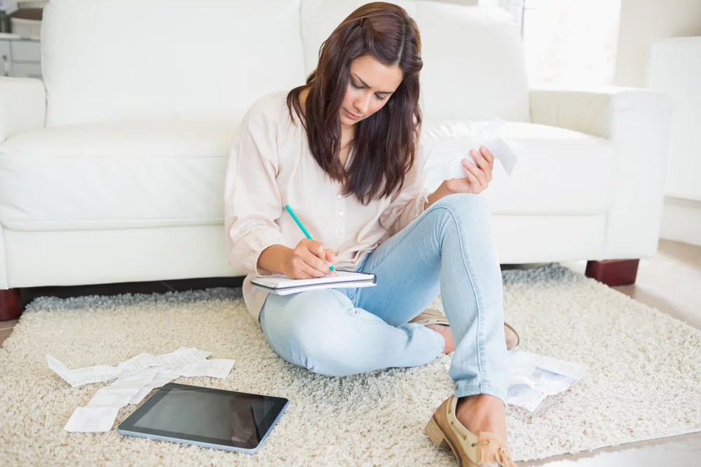 Young woman adding receipts on floor of living room