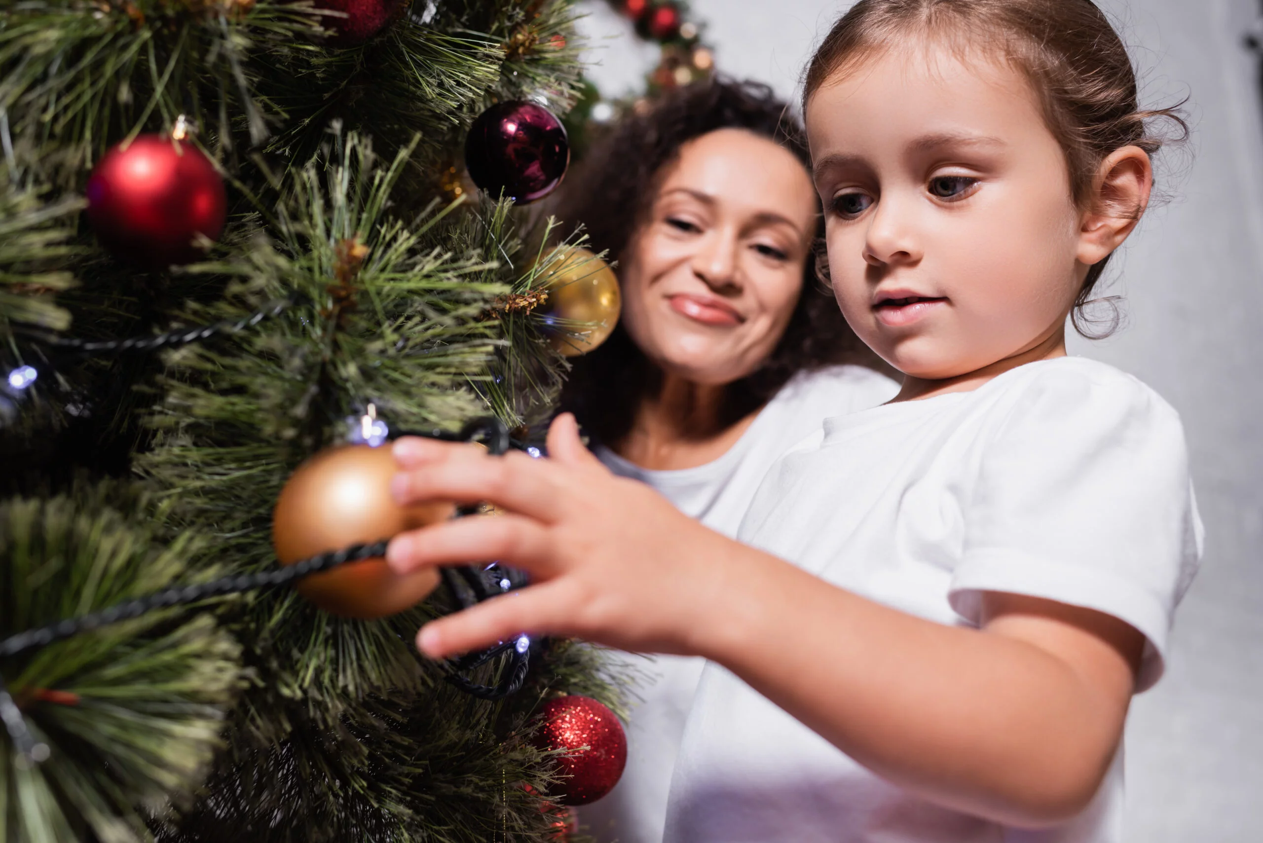 young girl with her mother decorating christmas tree