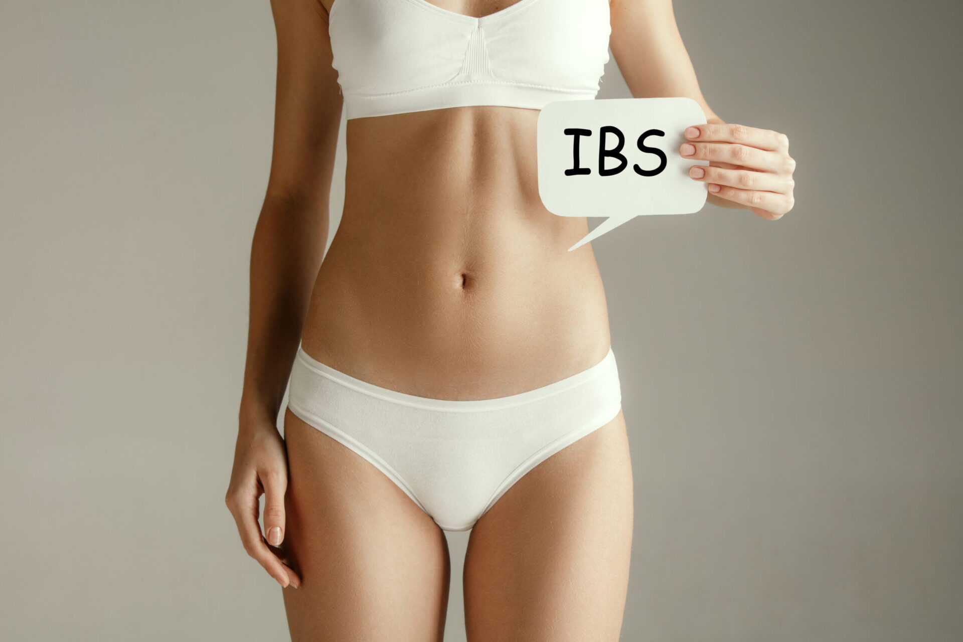 Stomach ache concept. The woman with text IBS on gray studio background. Irritable bowel syndrome or IBS