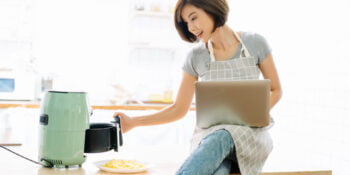 Portrait of beautiful Asian woman working on laptop while cooking with Air Fryers in kitchen