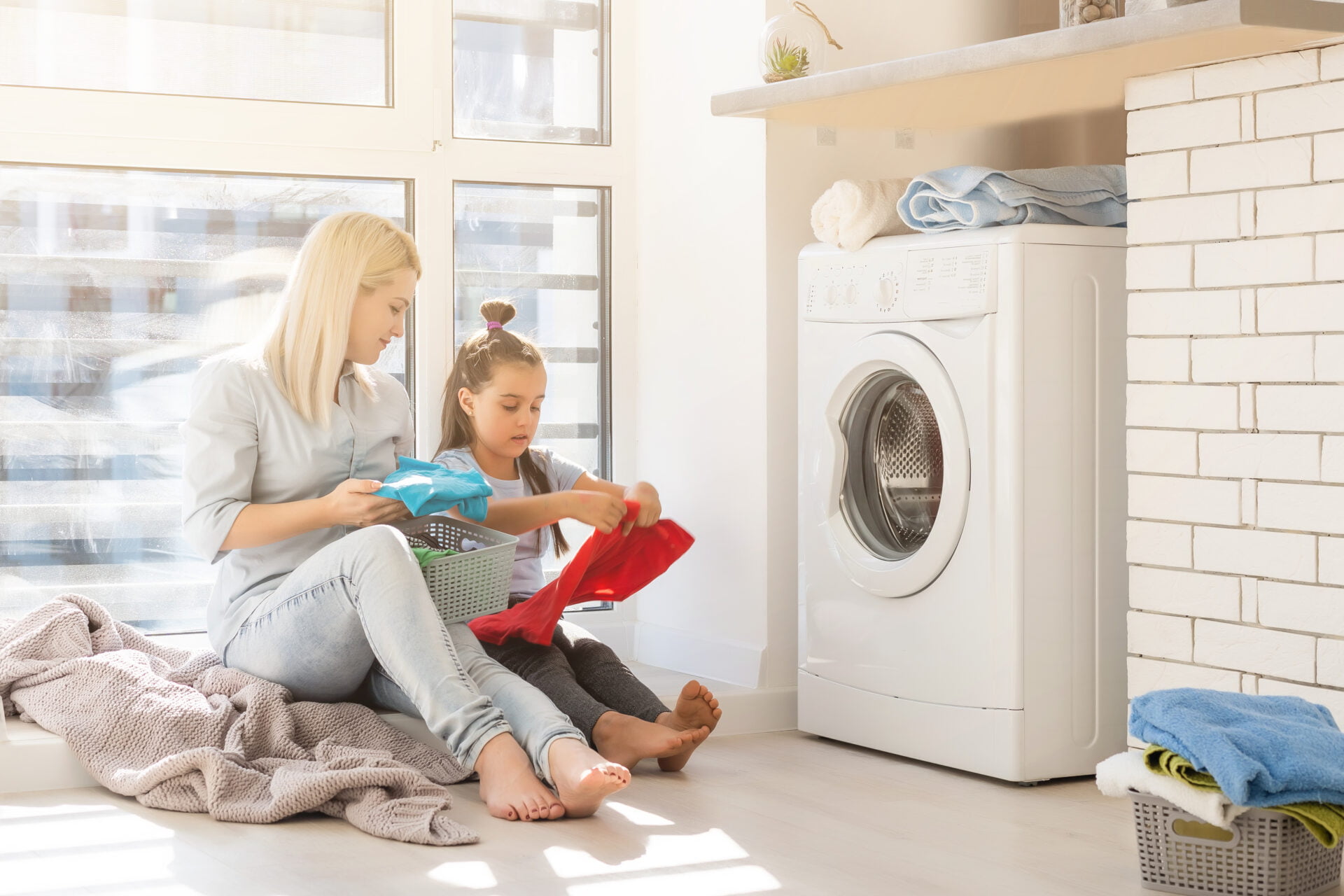 Happy housewife and her daughter with linen near washing machine