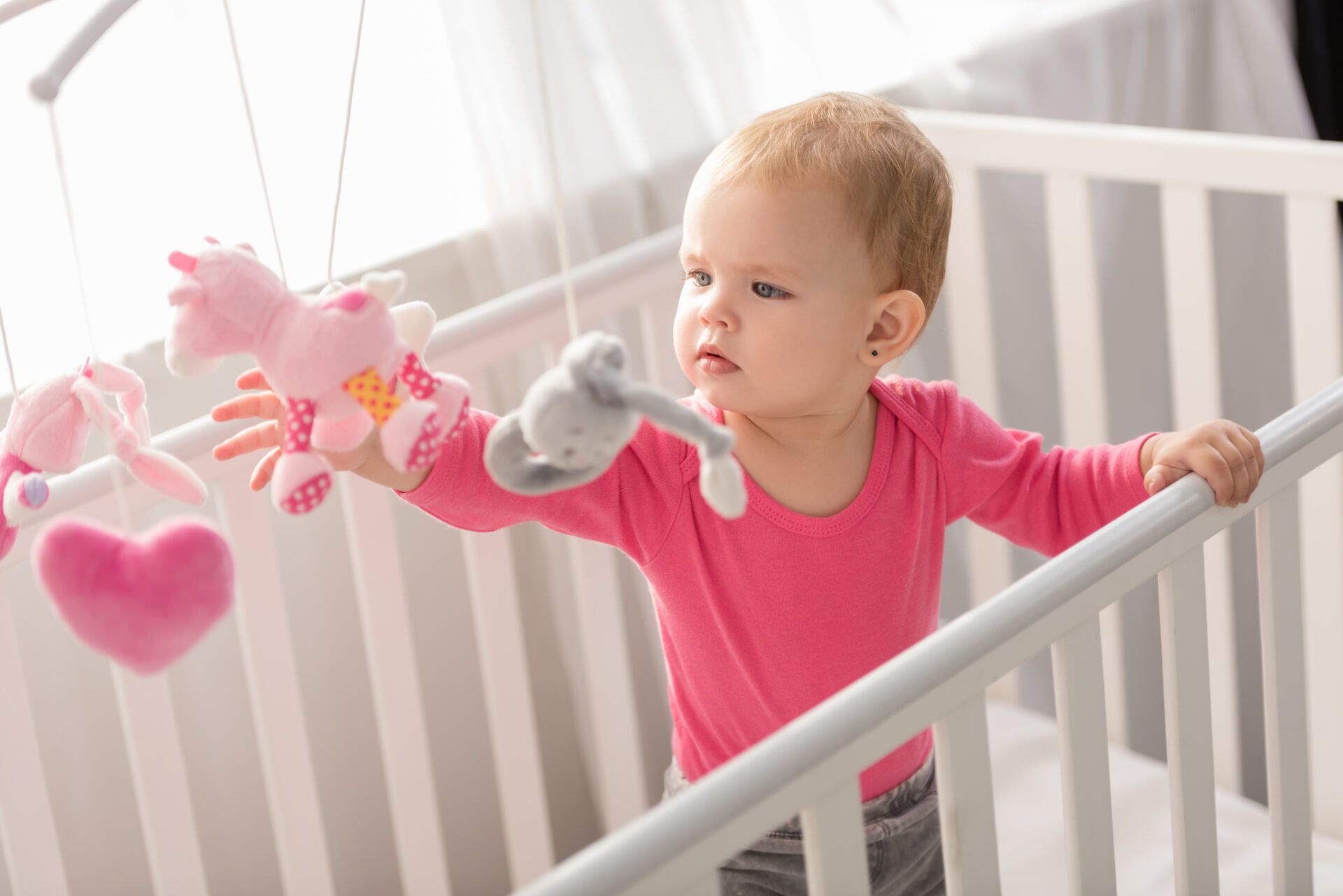 girl standing in her crib with pink shirt