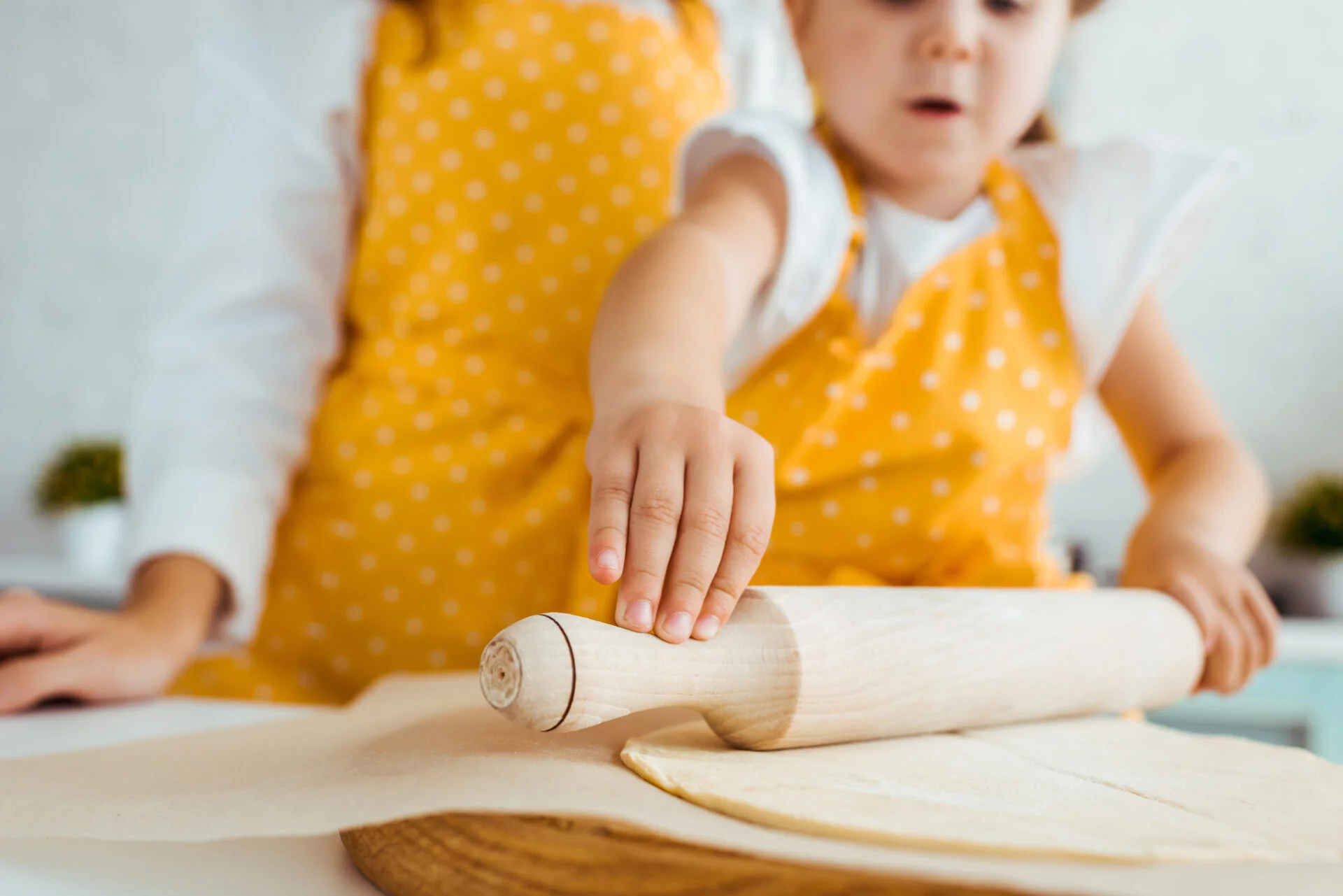 Mother and daughter rolling out dough on top of parchment paper