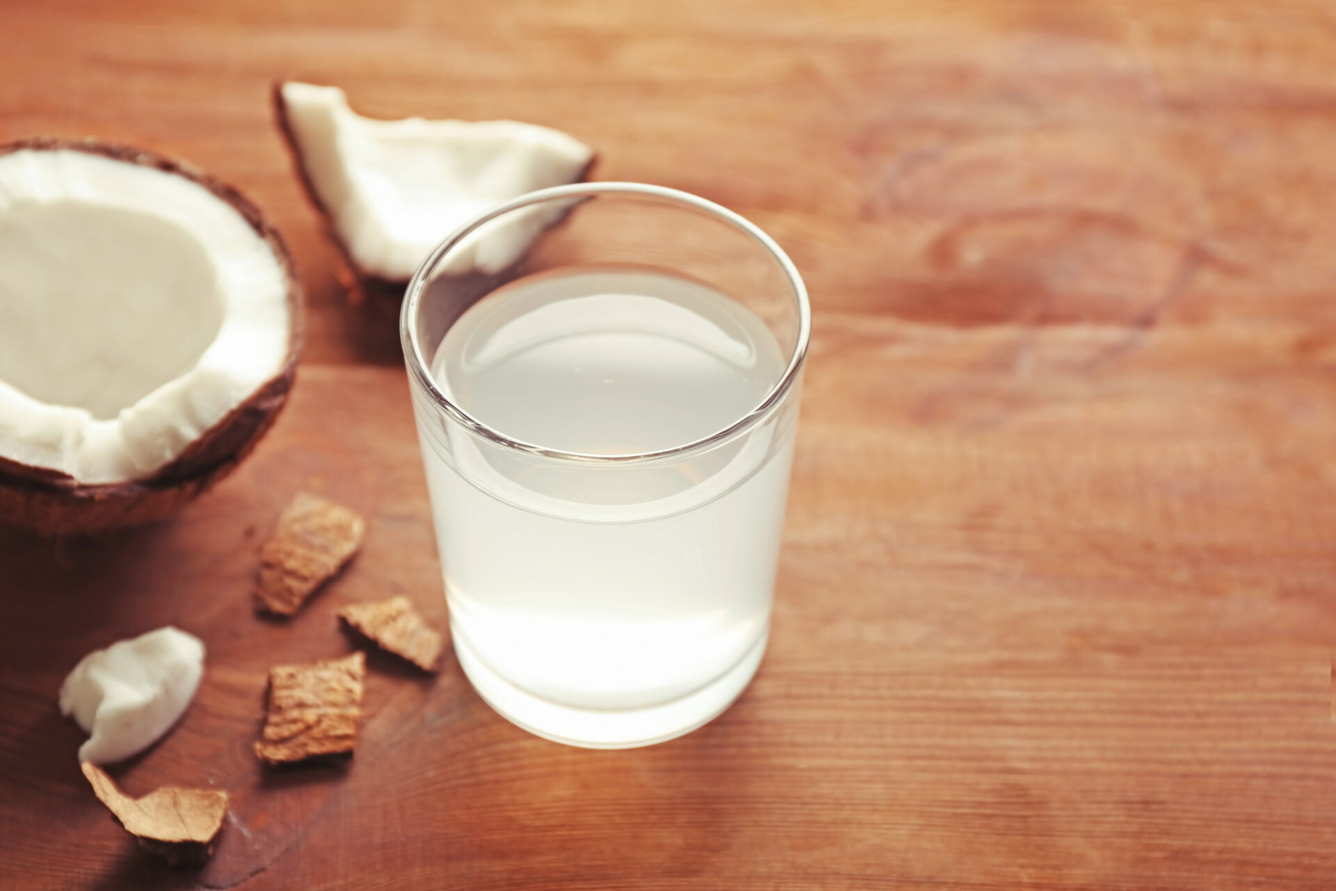 Glass of coconut water and fresh nut on wooden background